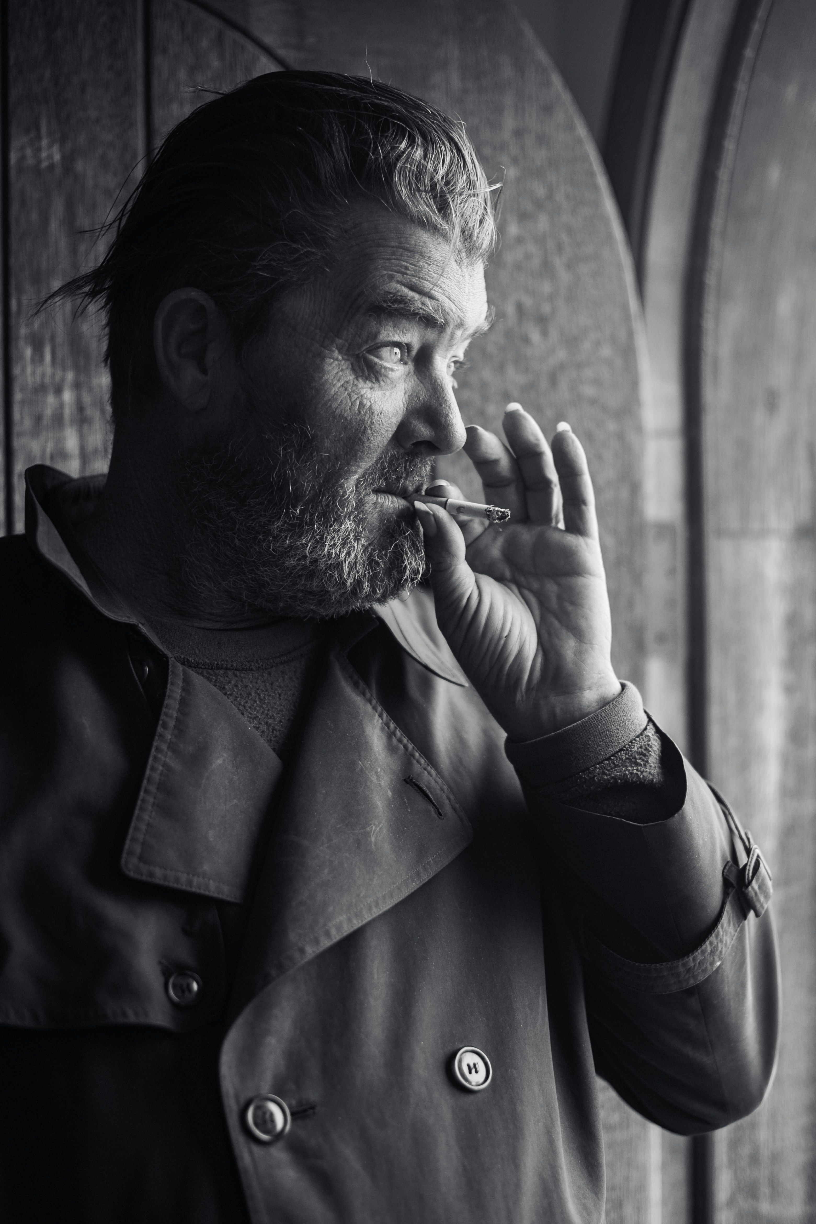 Uomo che fuma una sigaretta vicino a una finestra.