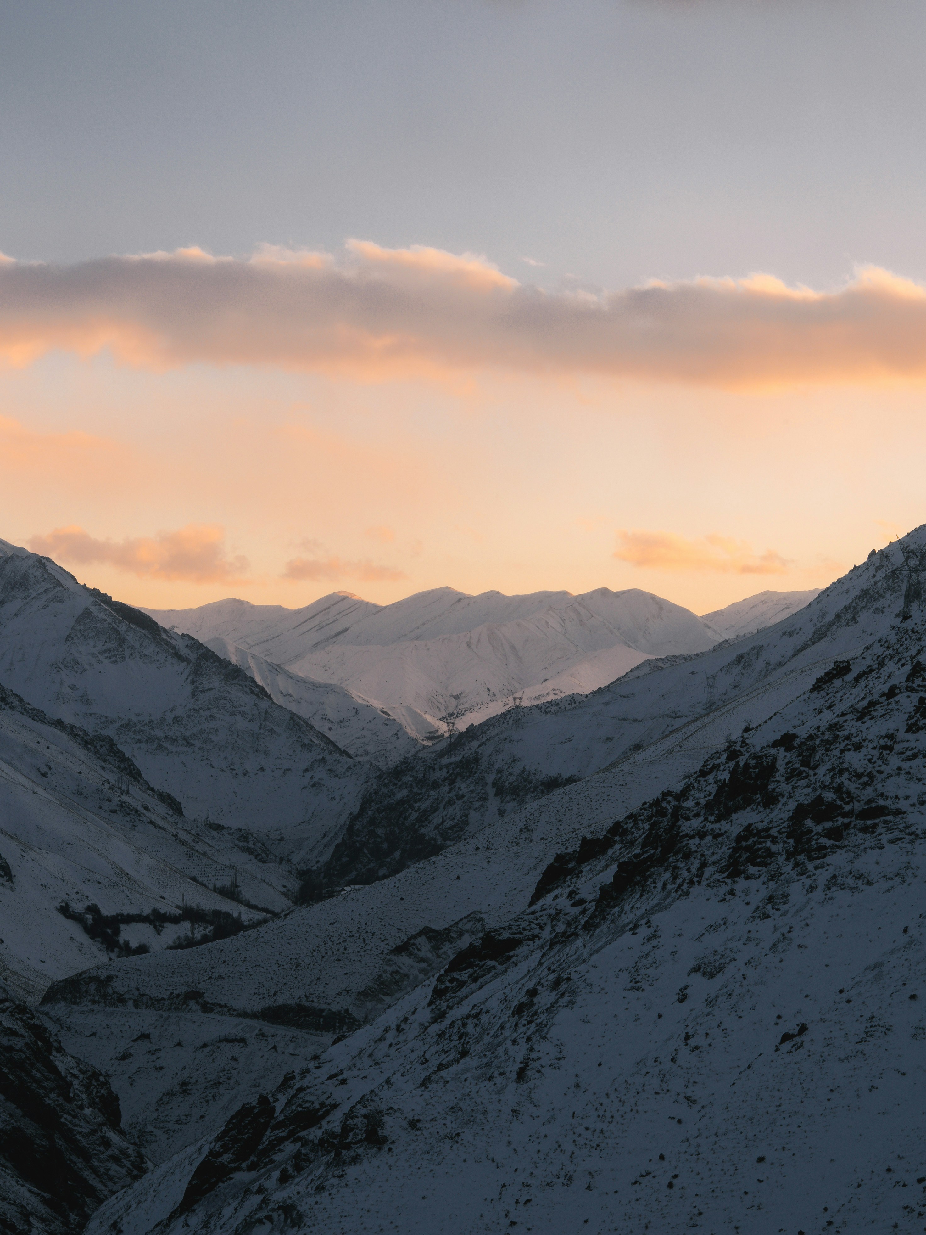 Snowy mountain valley at dusk with soft clouds.