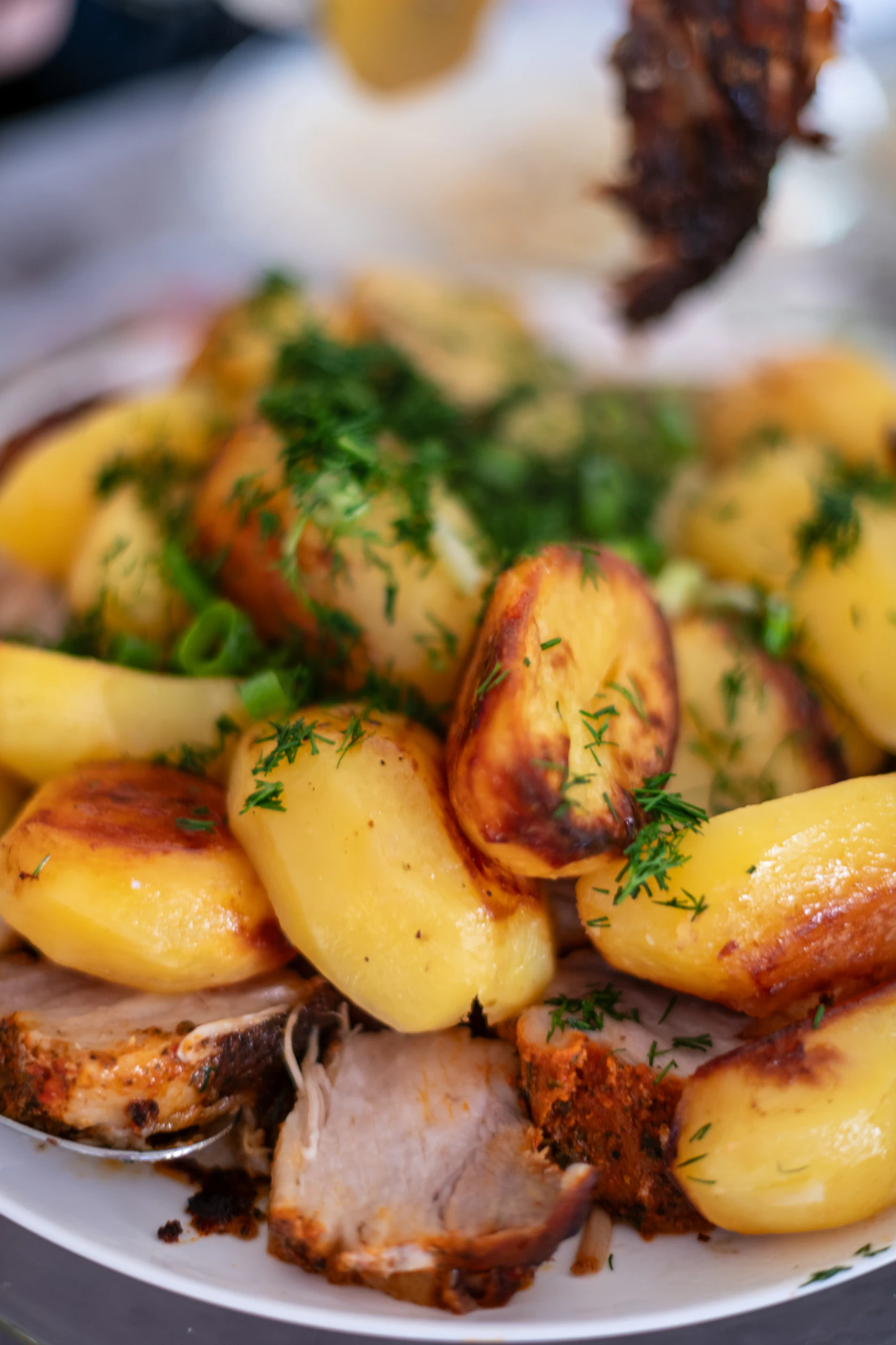 Sliced roasted pork with crispy potatoes and fresh dill on a serving platter