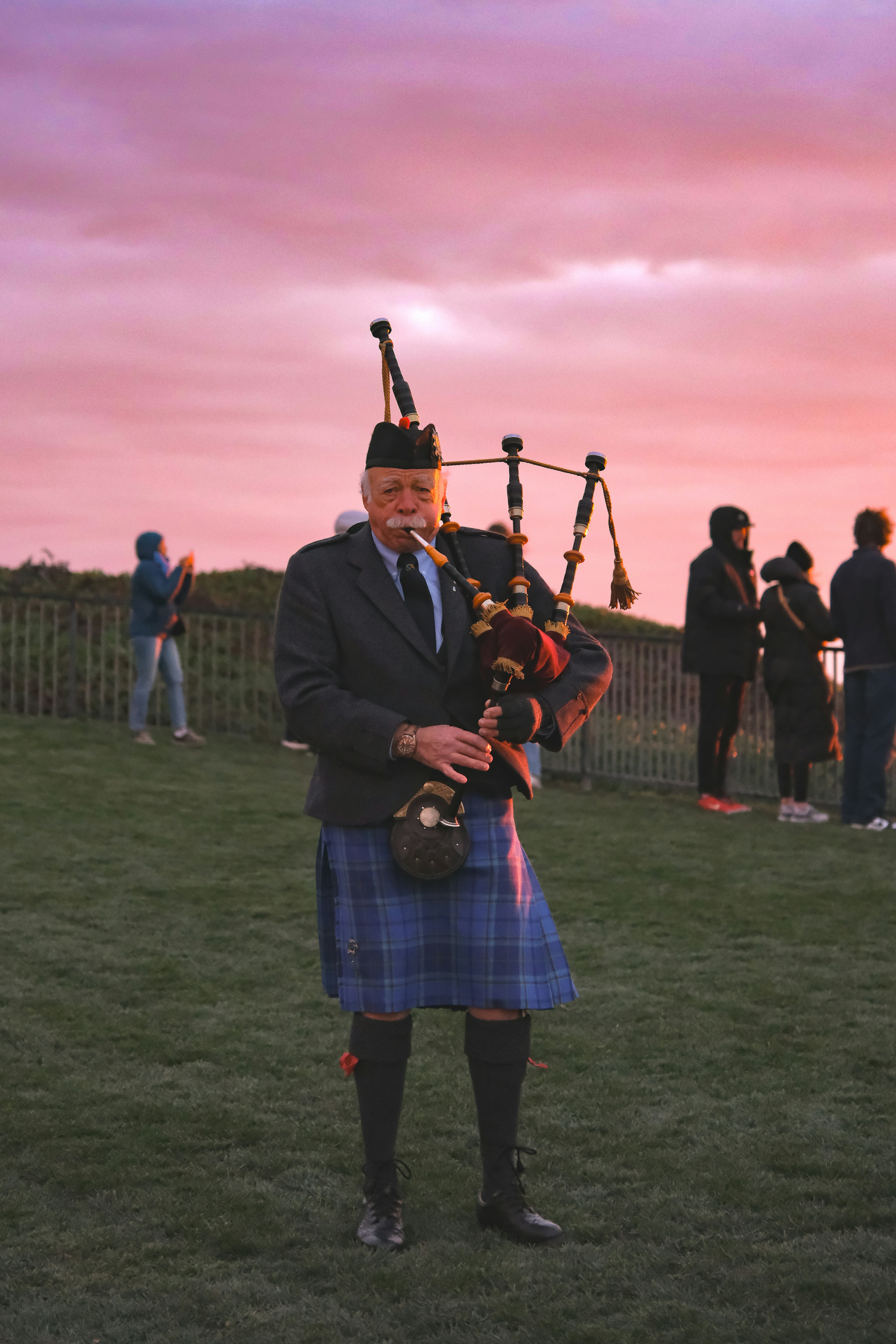 Homem de kilt toca gaita de foles ao pôr do sol