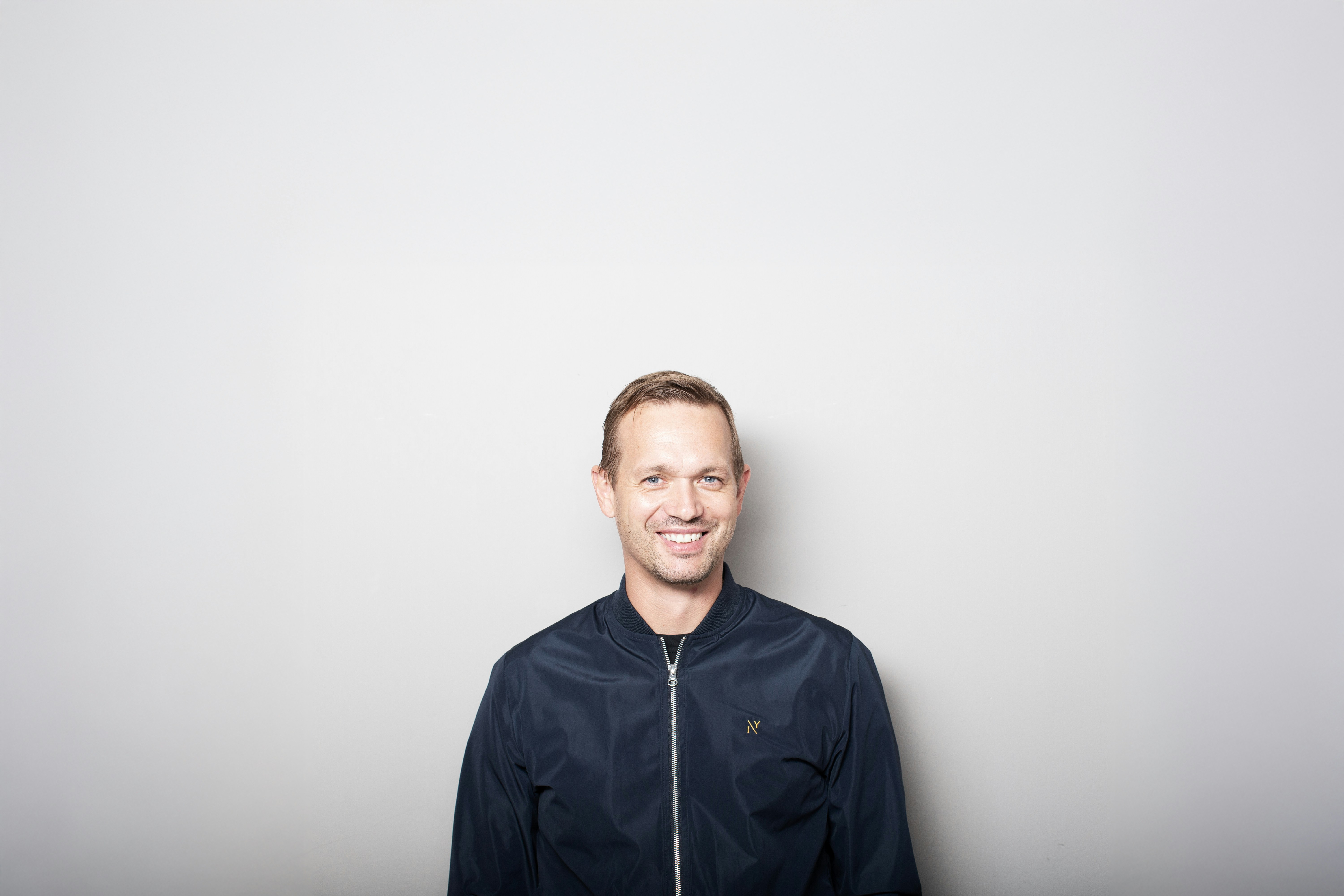 Smiling man in a dark jacket against a gray background.