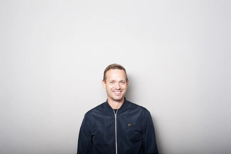 一位身穿深色夹克、面带微笑的男士，背景是灰色，沉稳而有魅力