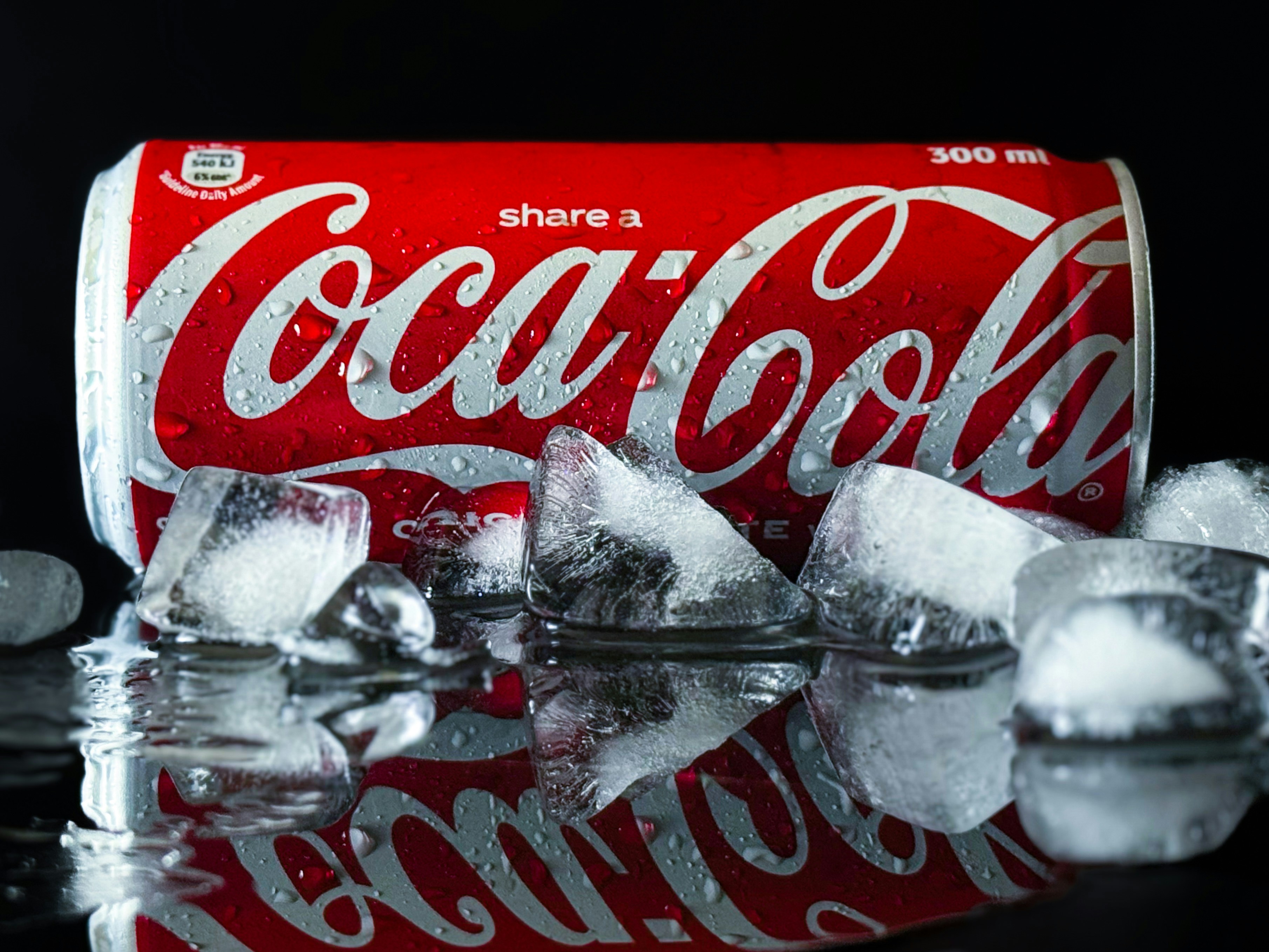 An ice cold can of Coca Cola with some ice cubes in the foreground