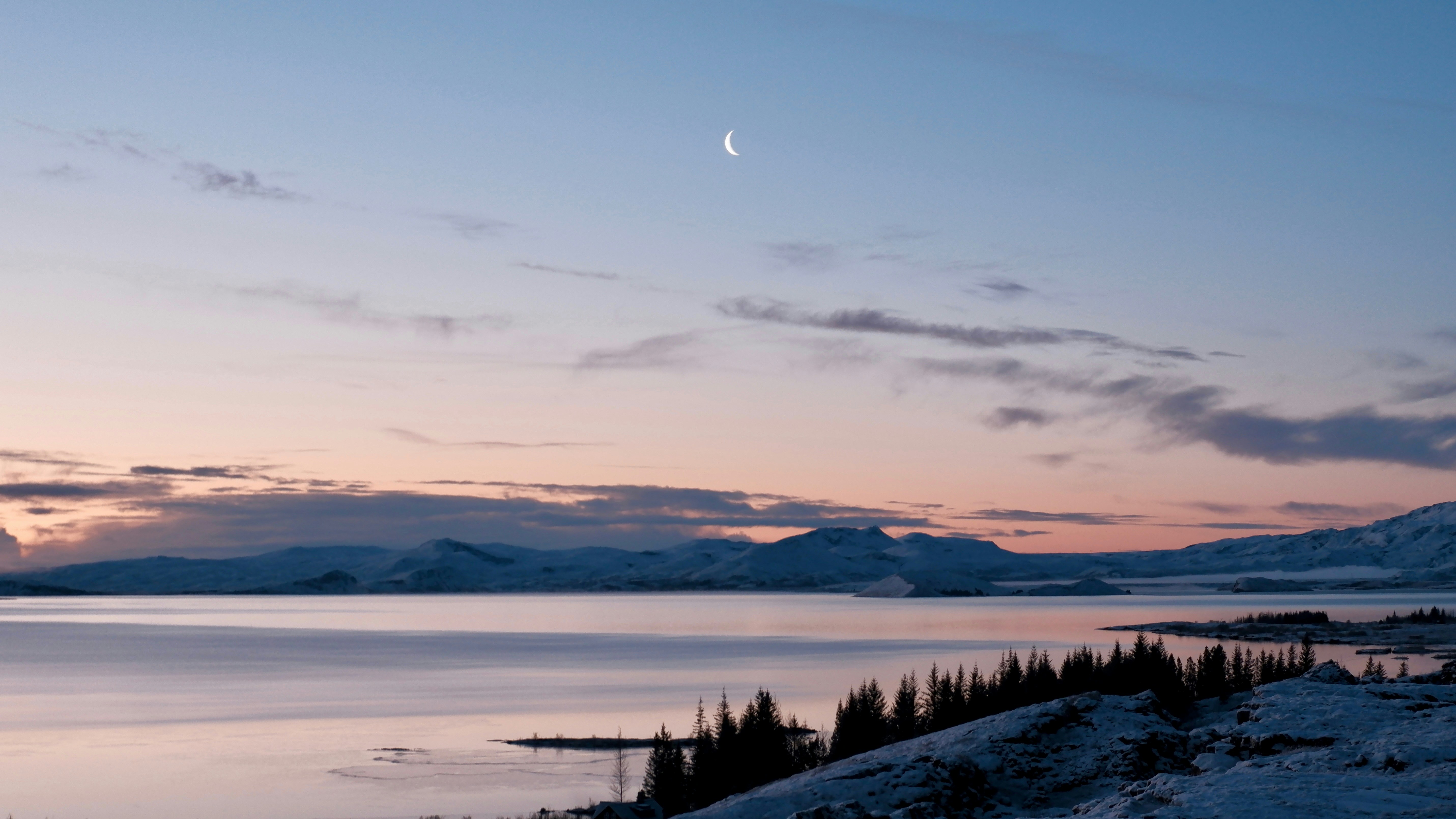 Luna crescente su un lago sereno al crepuscolo.