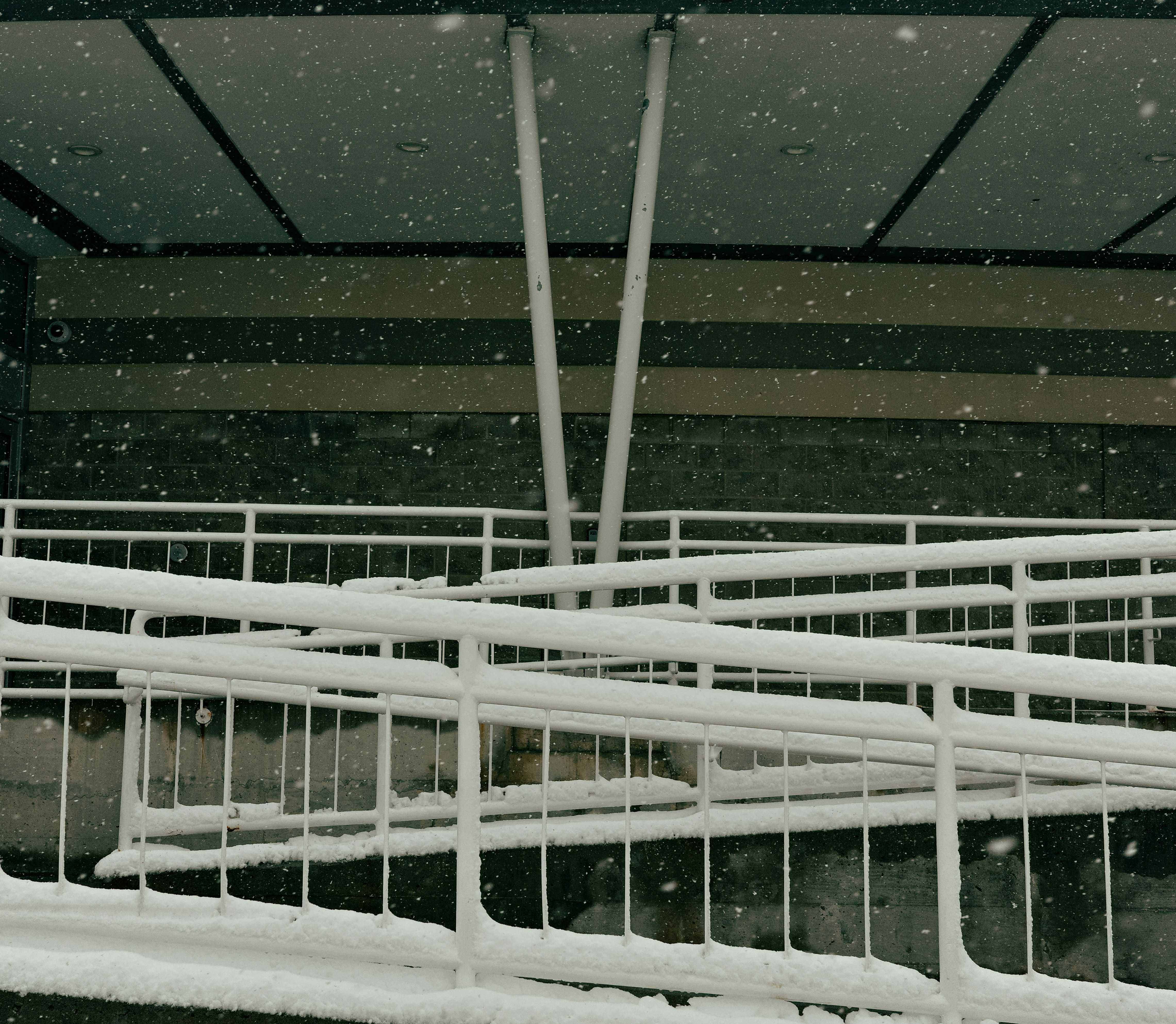 Snow falling on a white ramp and railing.