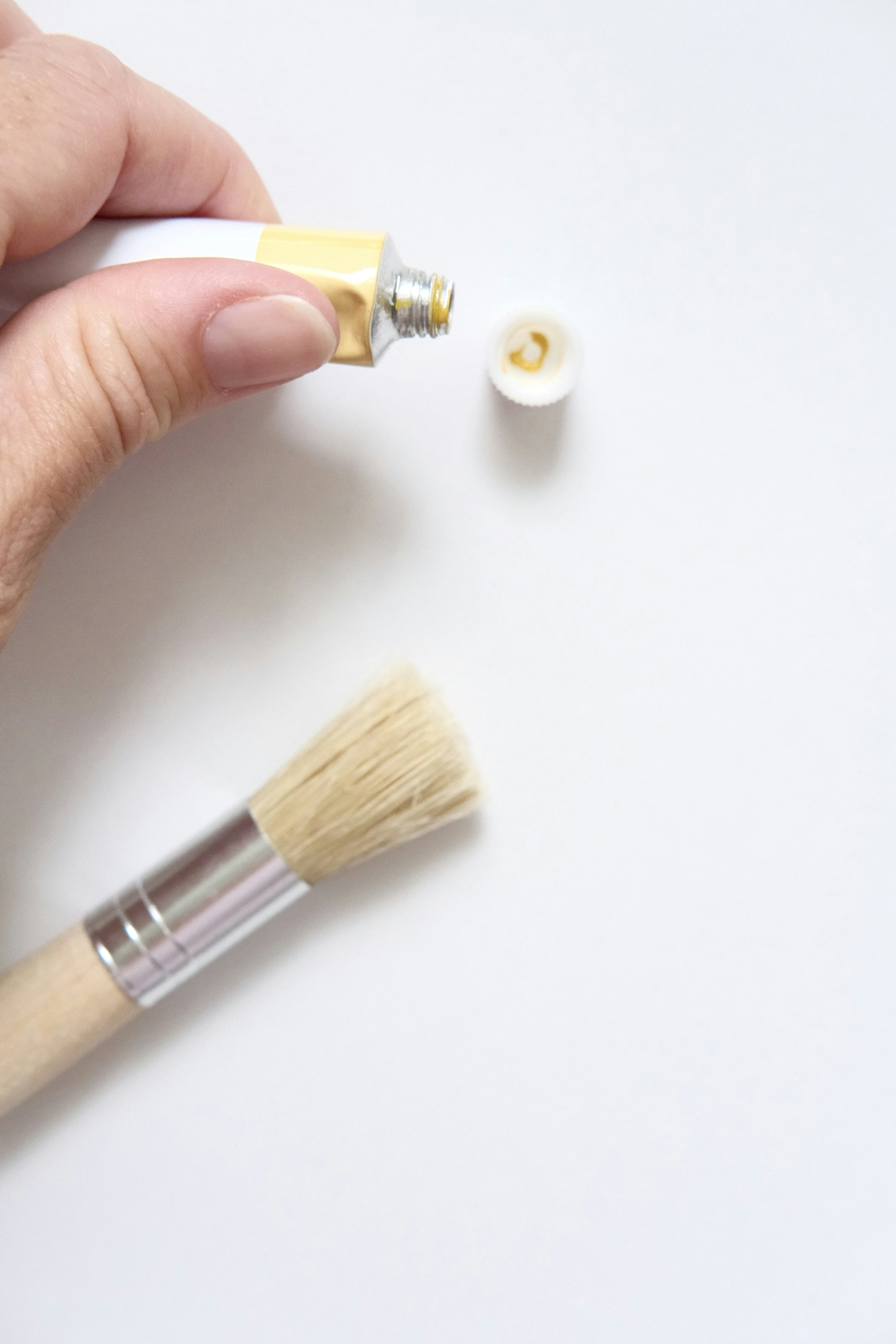 Hand squeezing yellow paint from tube onto brush