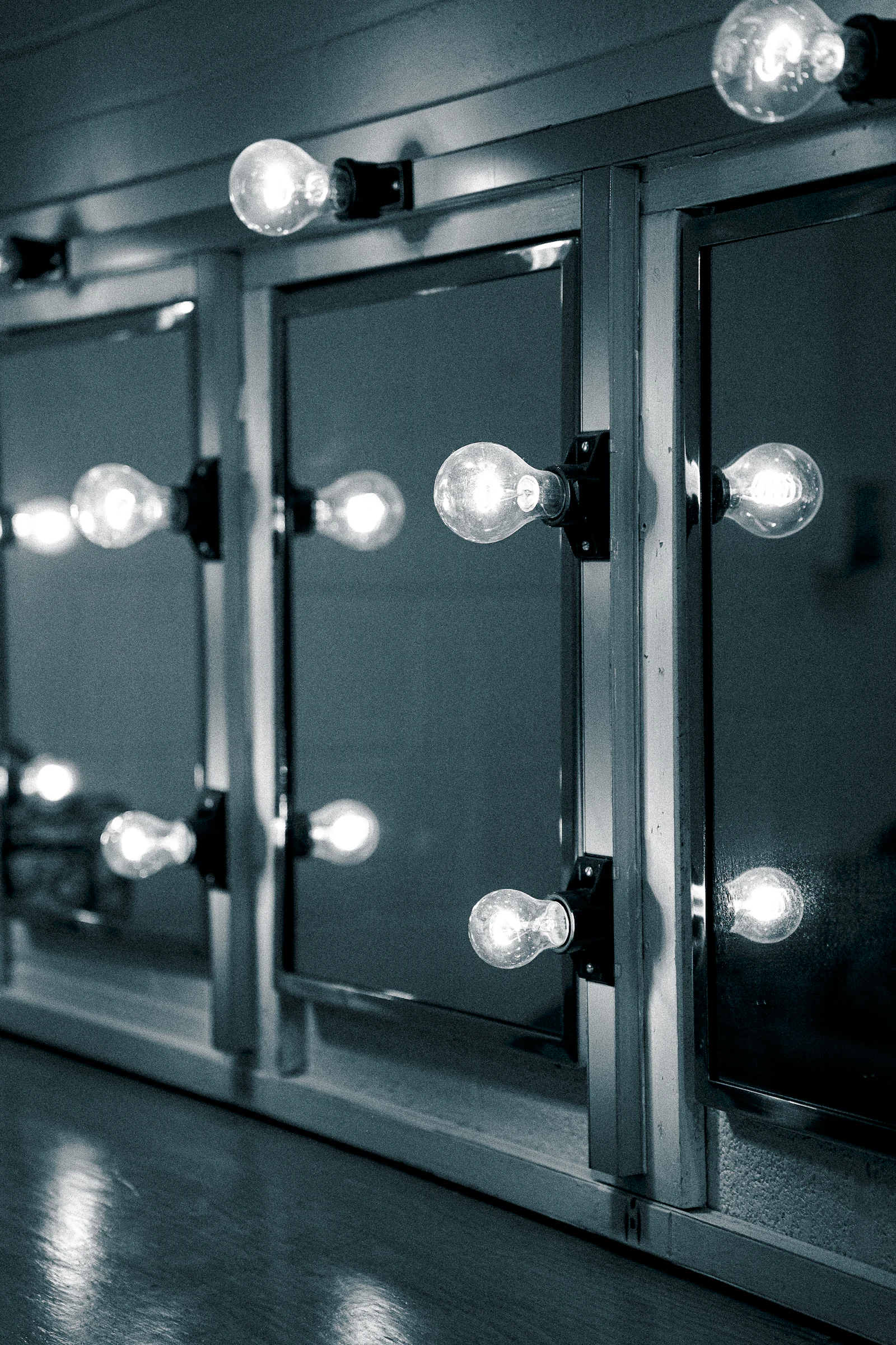 A row of bare bulbs burning along the edge of dressing room mirrors.