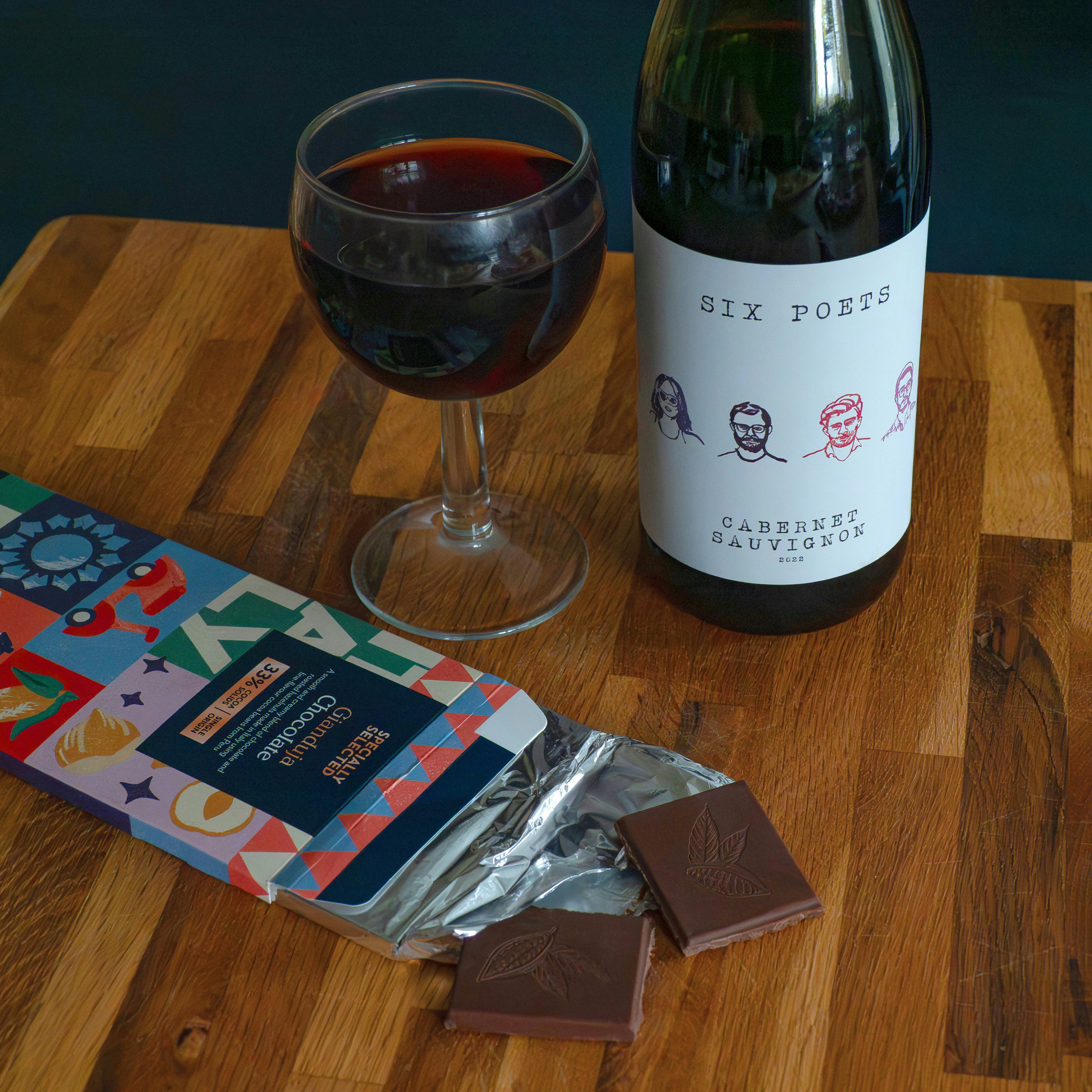 A glass of red wine with chocolate and a bottle.