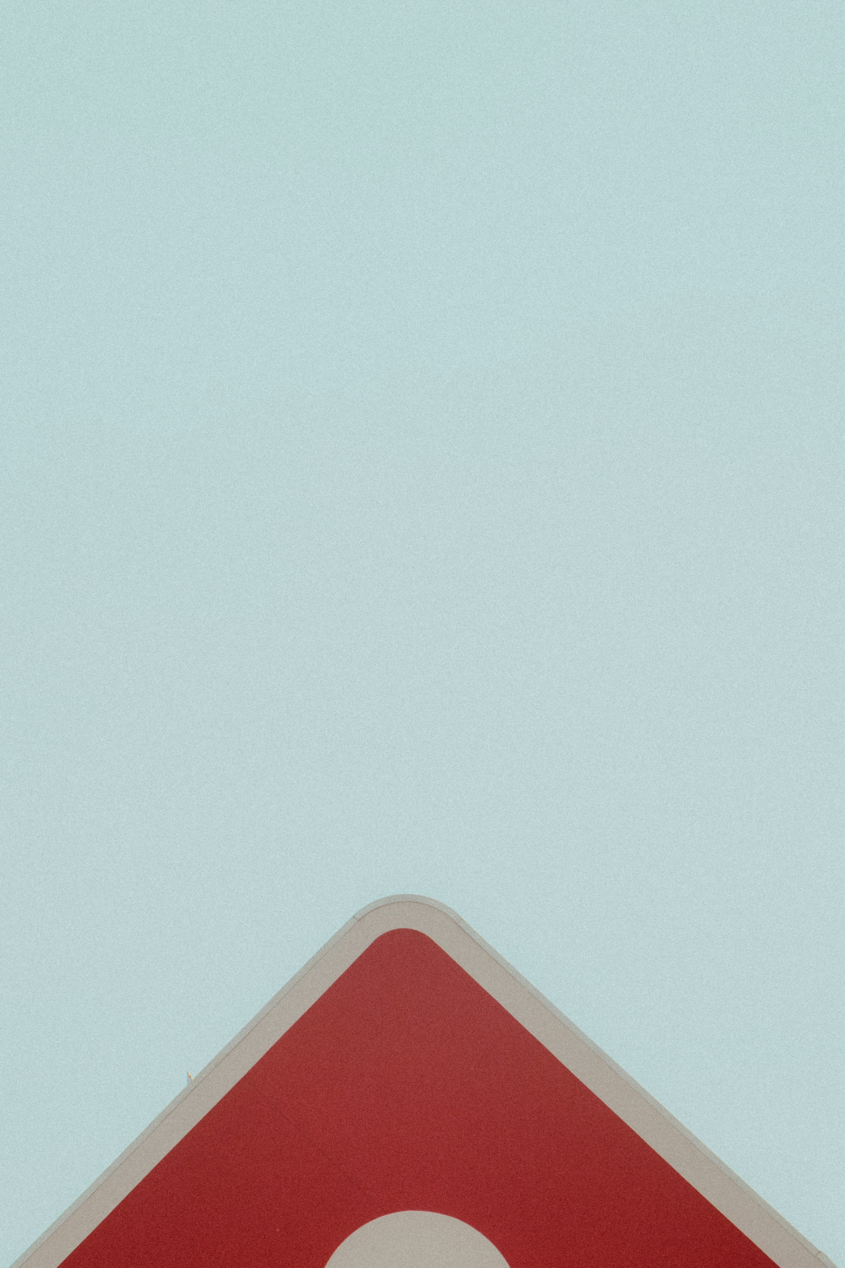 Red and white triangular sign against sky