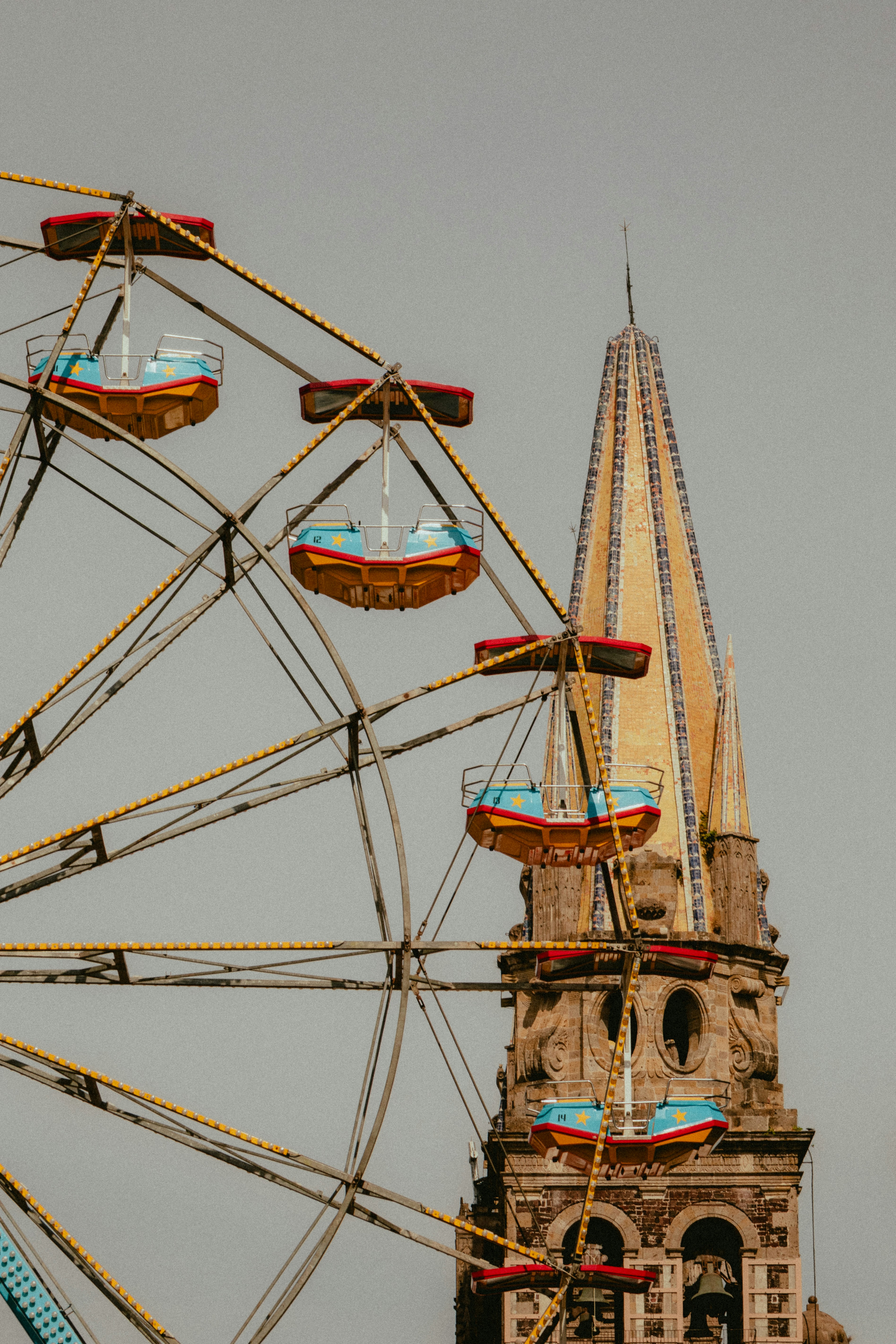 Ferris wheel and church tower against pale sky