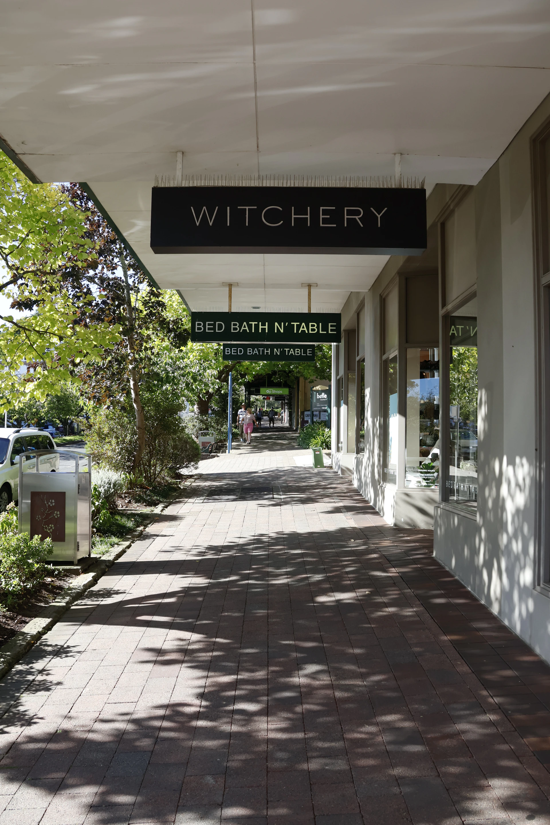 Shaded sidewalk outside shops with signs