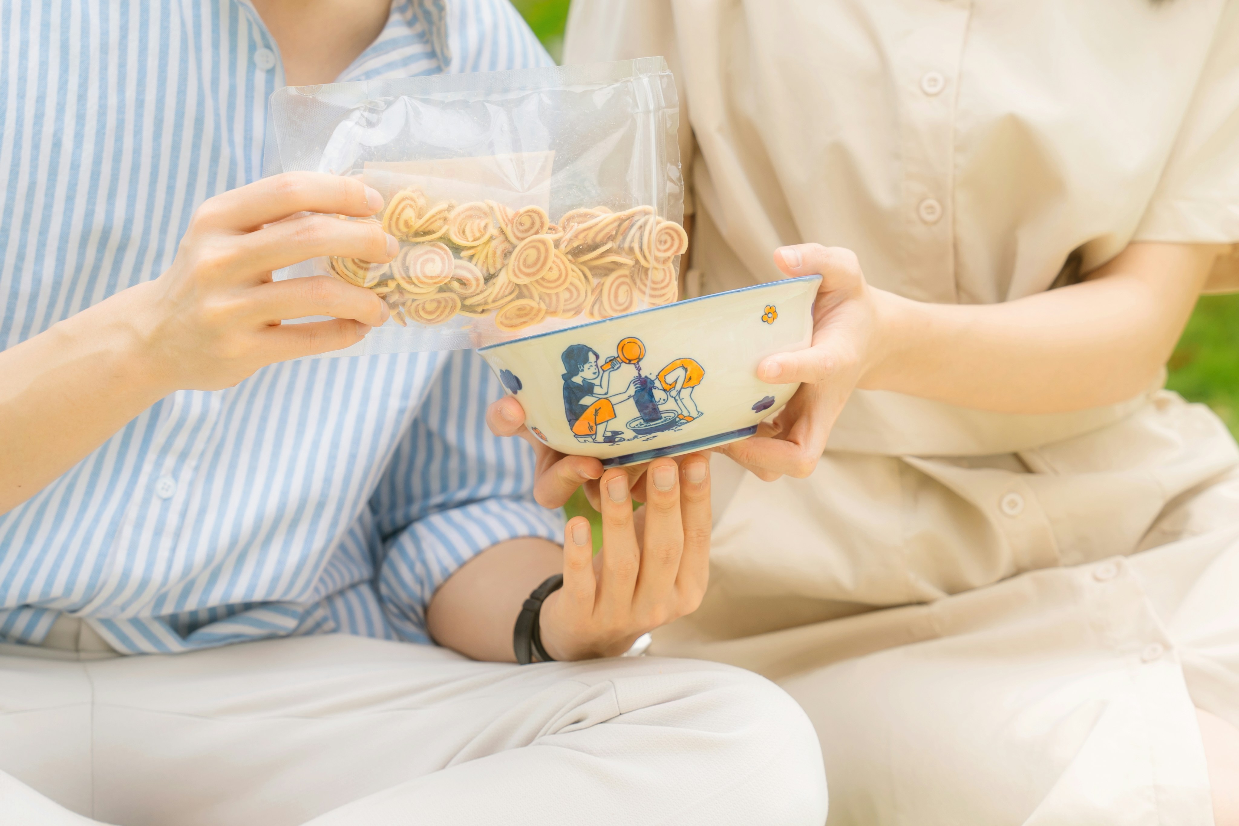 Two people sharing snacks from a bowl outdoors