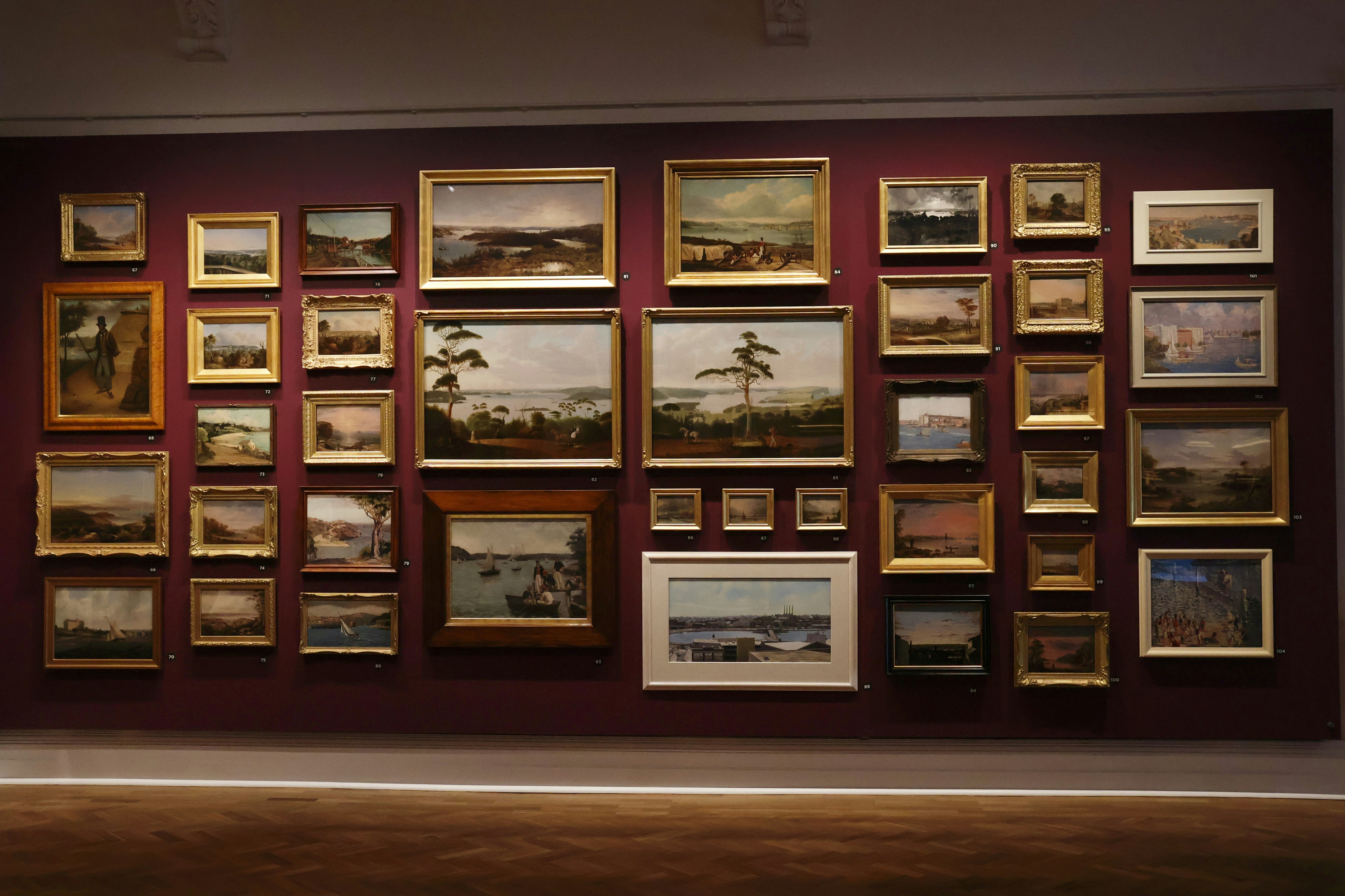 Sammlung von Landschaftsgemälden, die an einer Wand ausgestellt sind.