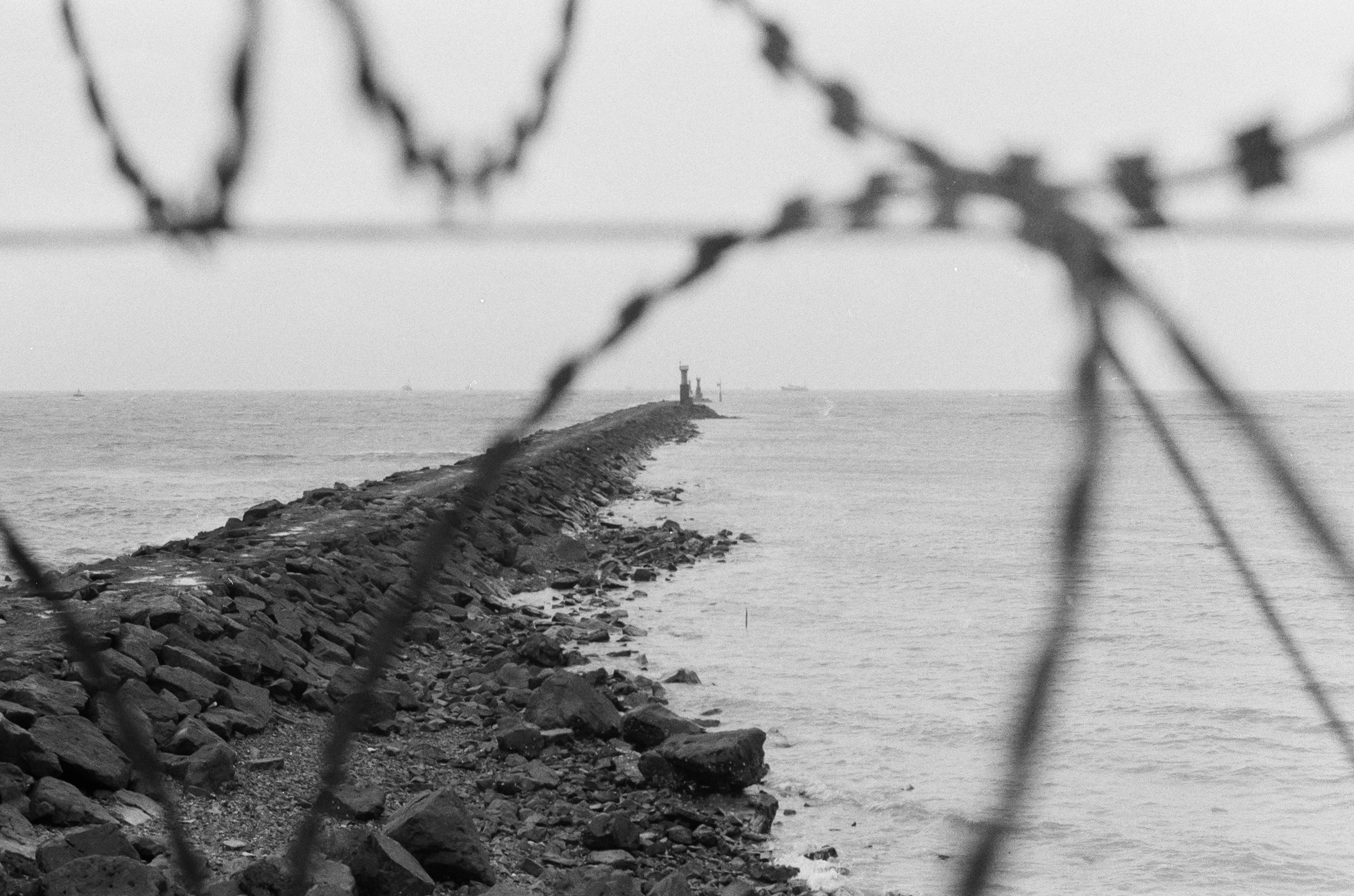Rocky pier with lighthouse and barbed wire foreground
