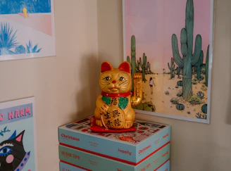 Lucky cat figurine on stack of boxes with desert art.