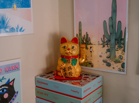 Lucky cat figurine on stack of boxes with desert art.