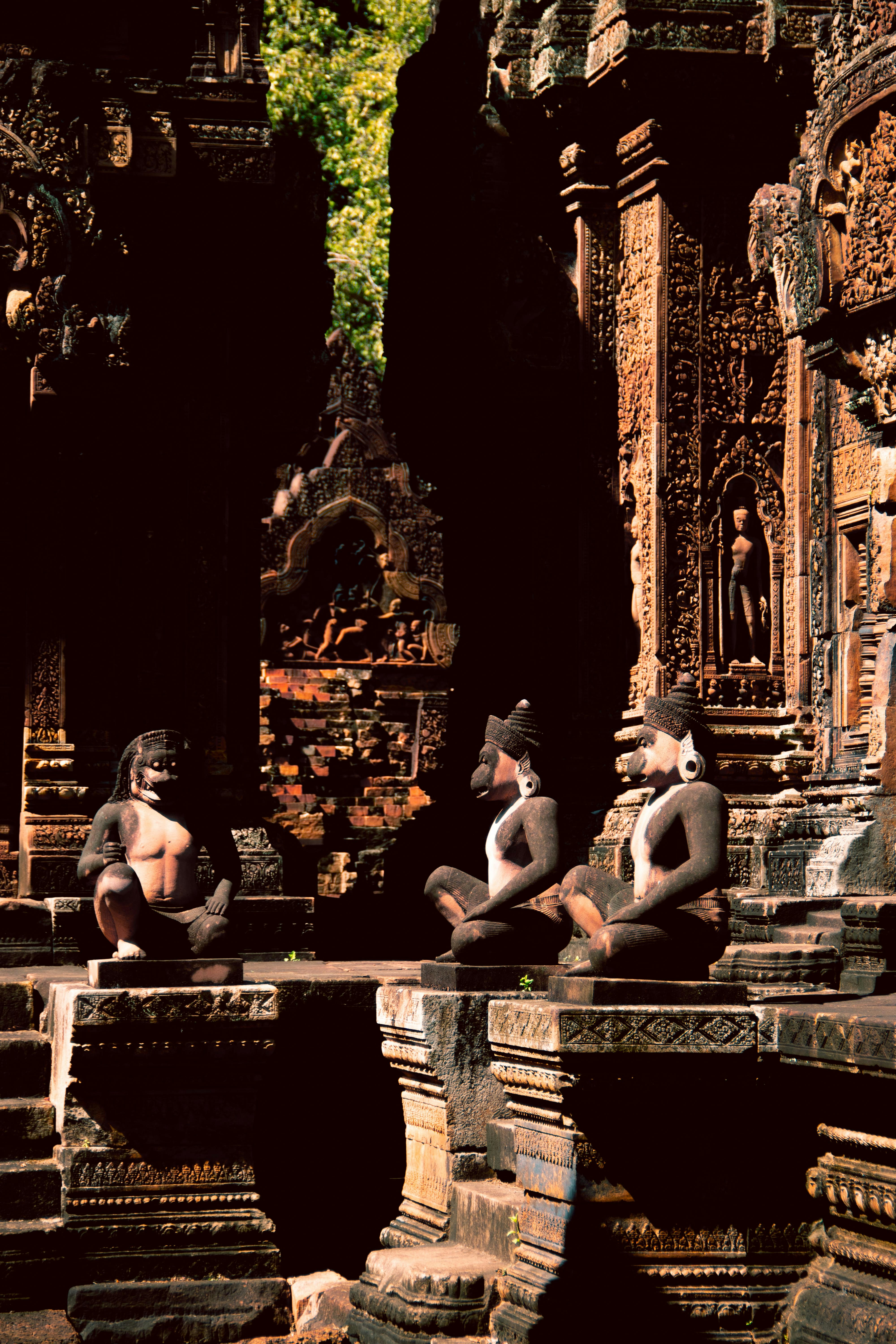 Three stone statues sit in front of ancient temple ruins.