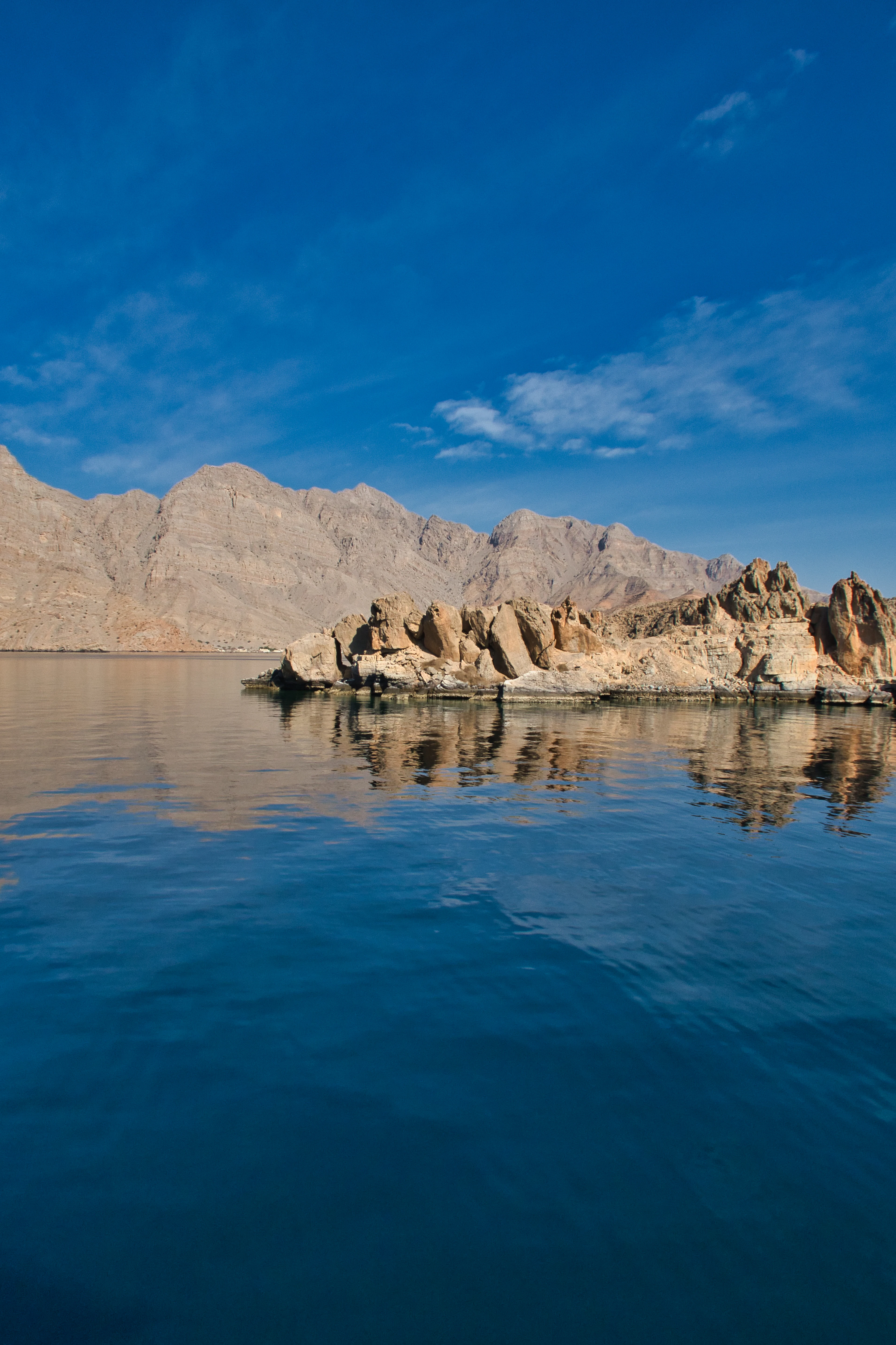 A rocky islet in a calm sea with mountains behind in golden-hour light near Khasab, Musandam