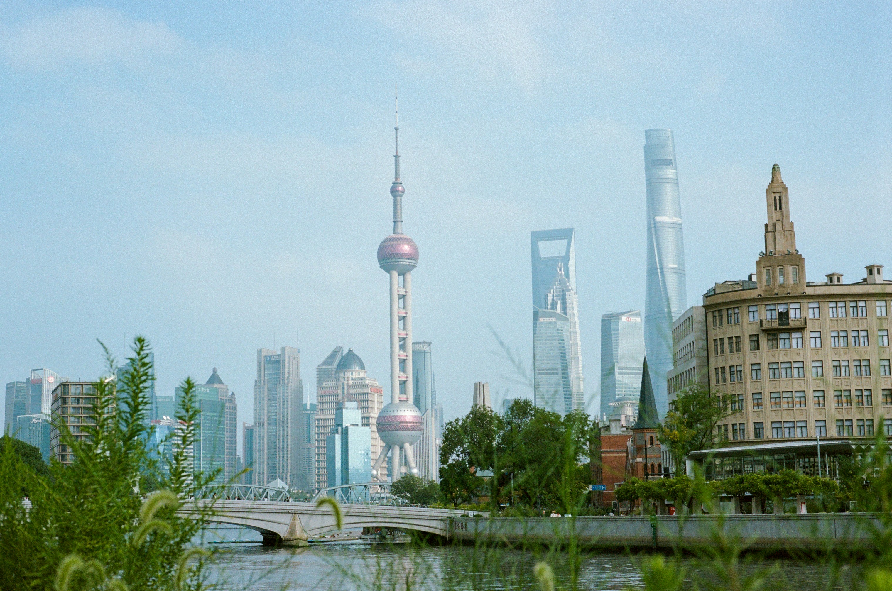 Modern cityscape with a river and lush greenery.