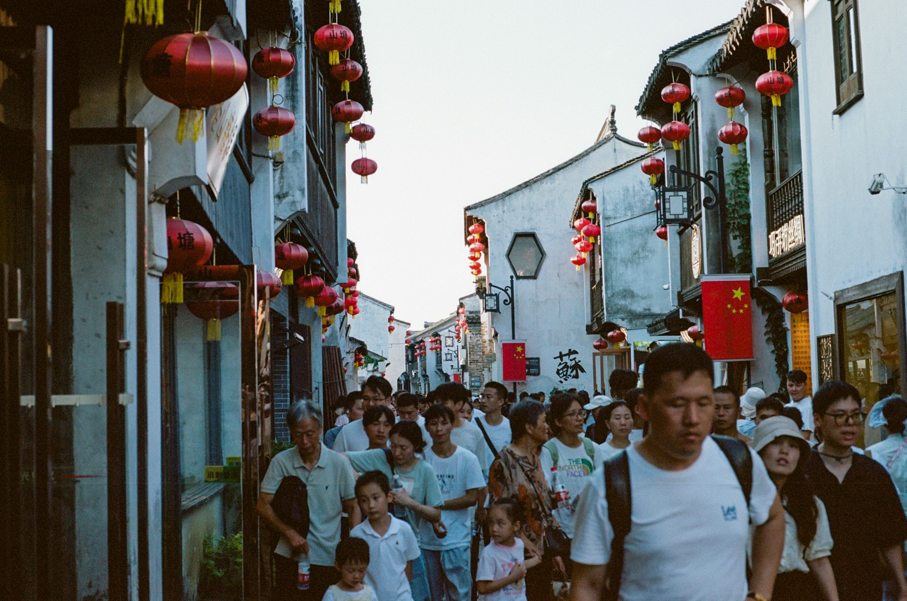 Crowd of people walking down a street lined with lanterns.