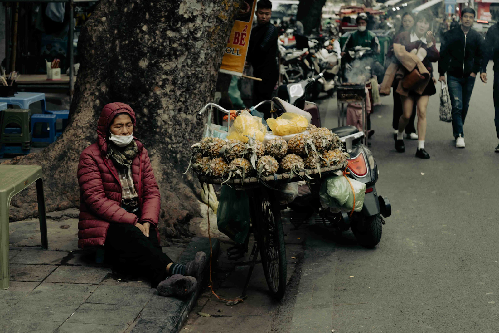 A woman sells fresh pineapples and produce from an outdoor market stall in the midday sun in Hanoi, Vietnam.