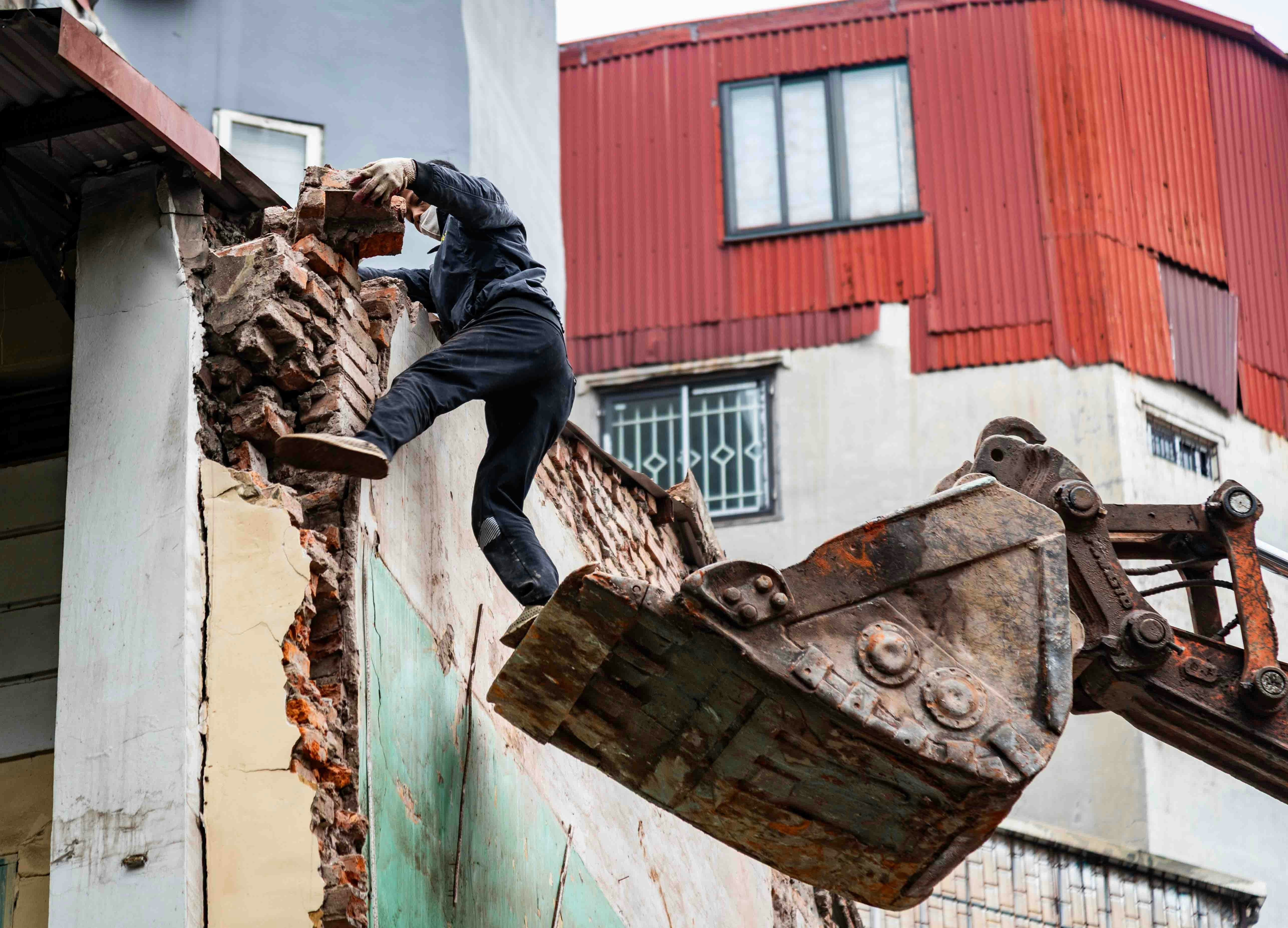 Worker demolishes building with excavator bucket