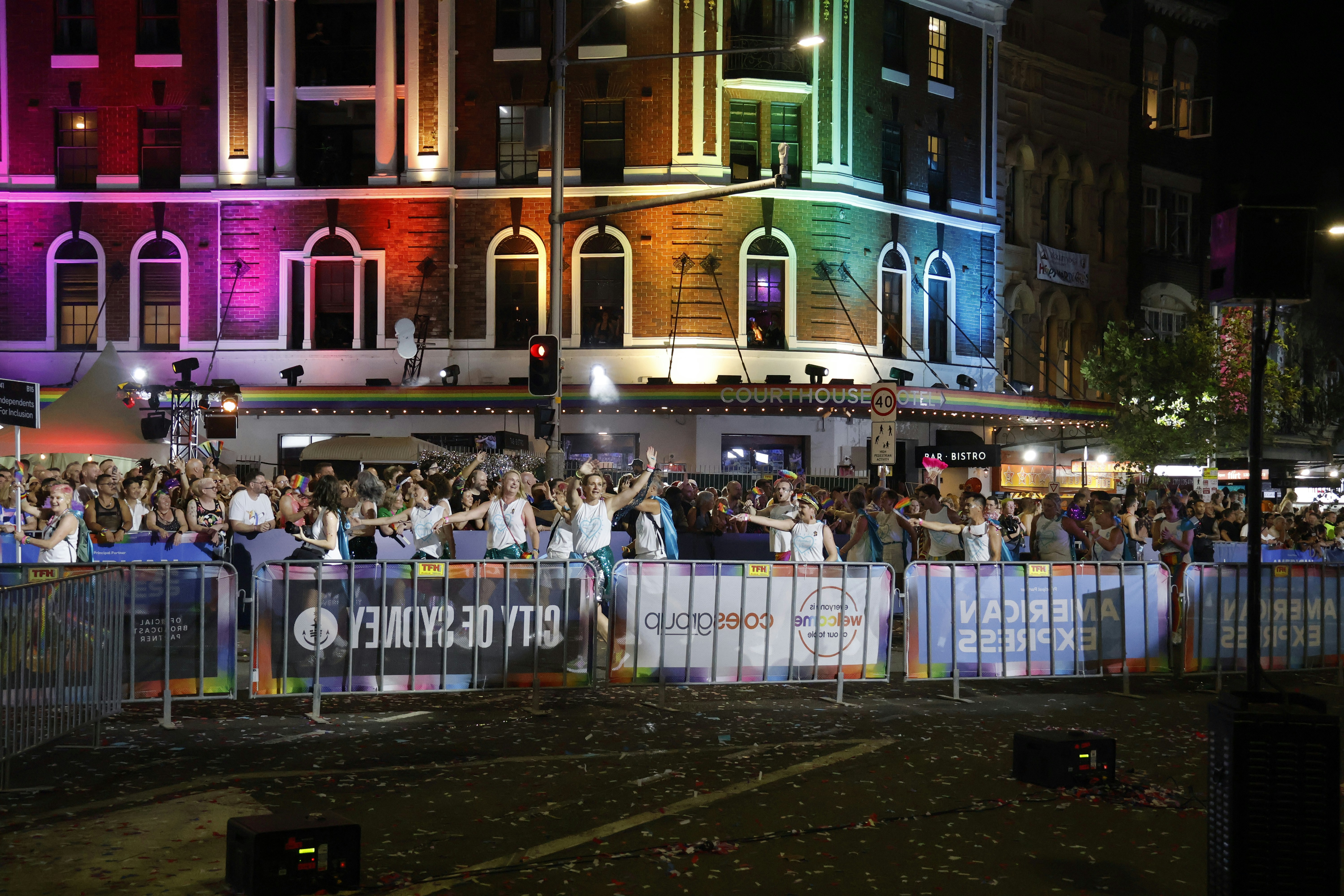 Crowd gathered on street with building lit by rainbow lights