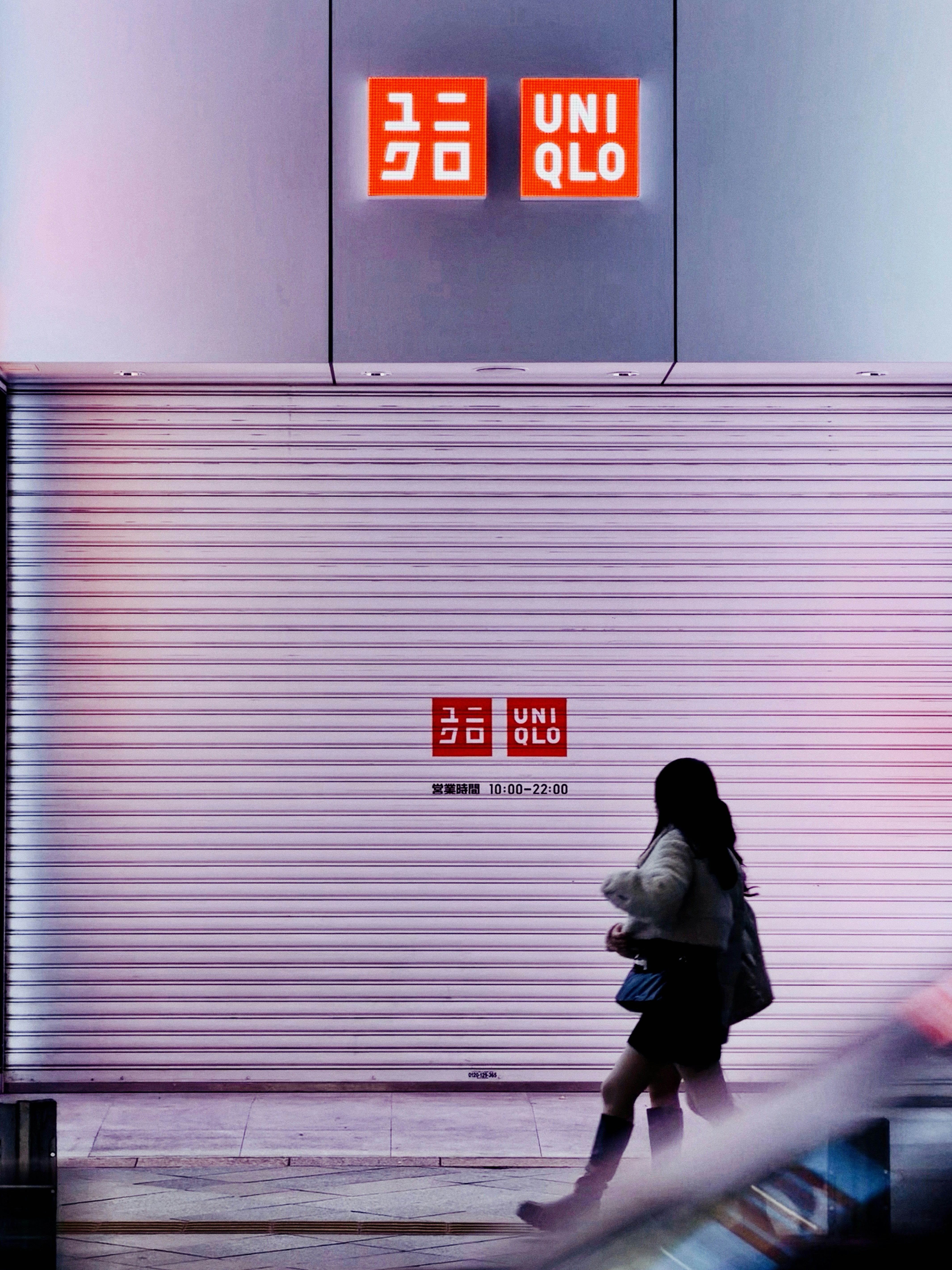Two people walk past a closed uniqlo store at night.