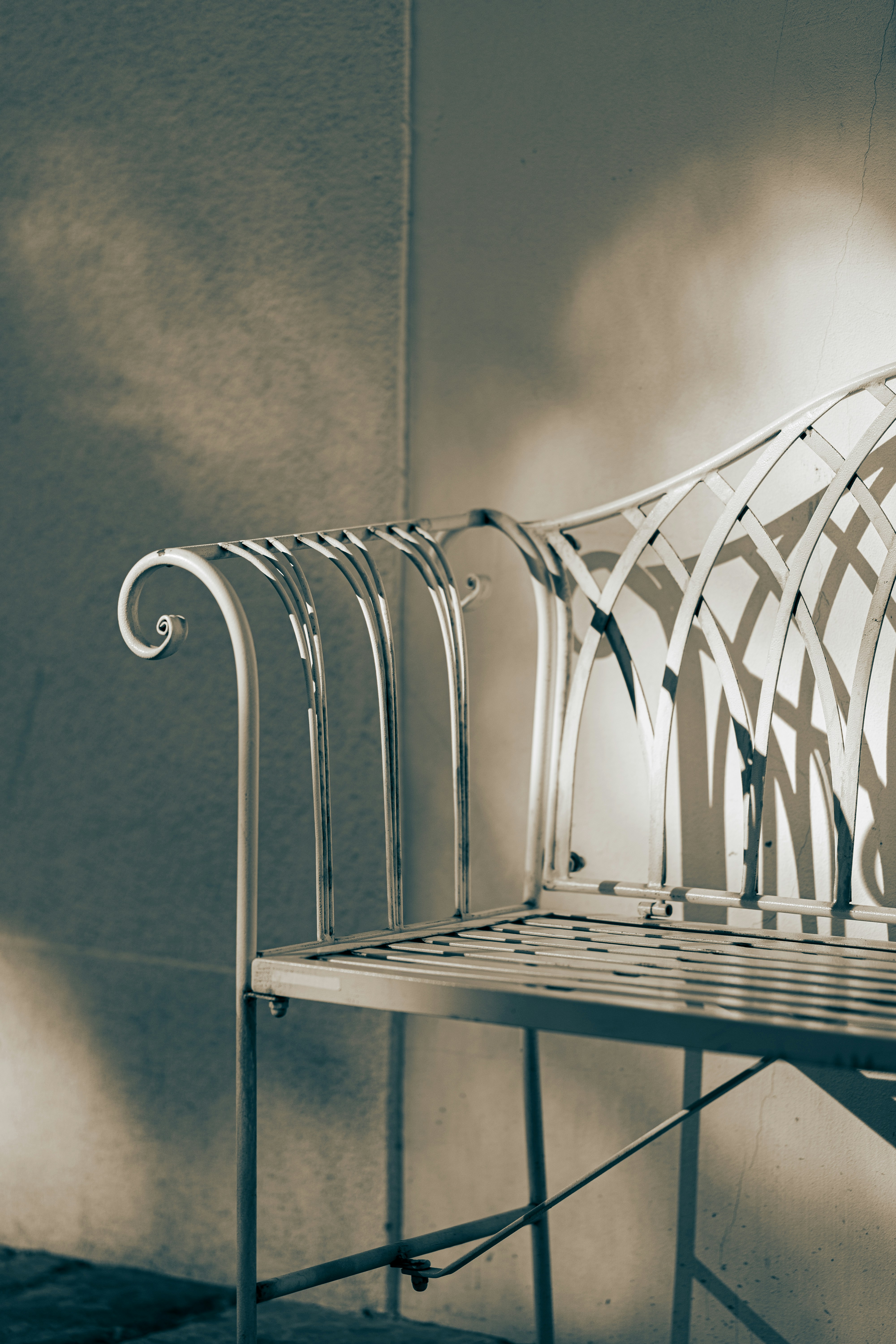 Banco de metal ornamentado projeta sombras contra a parede