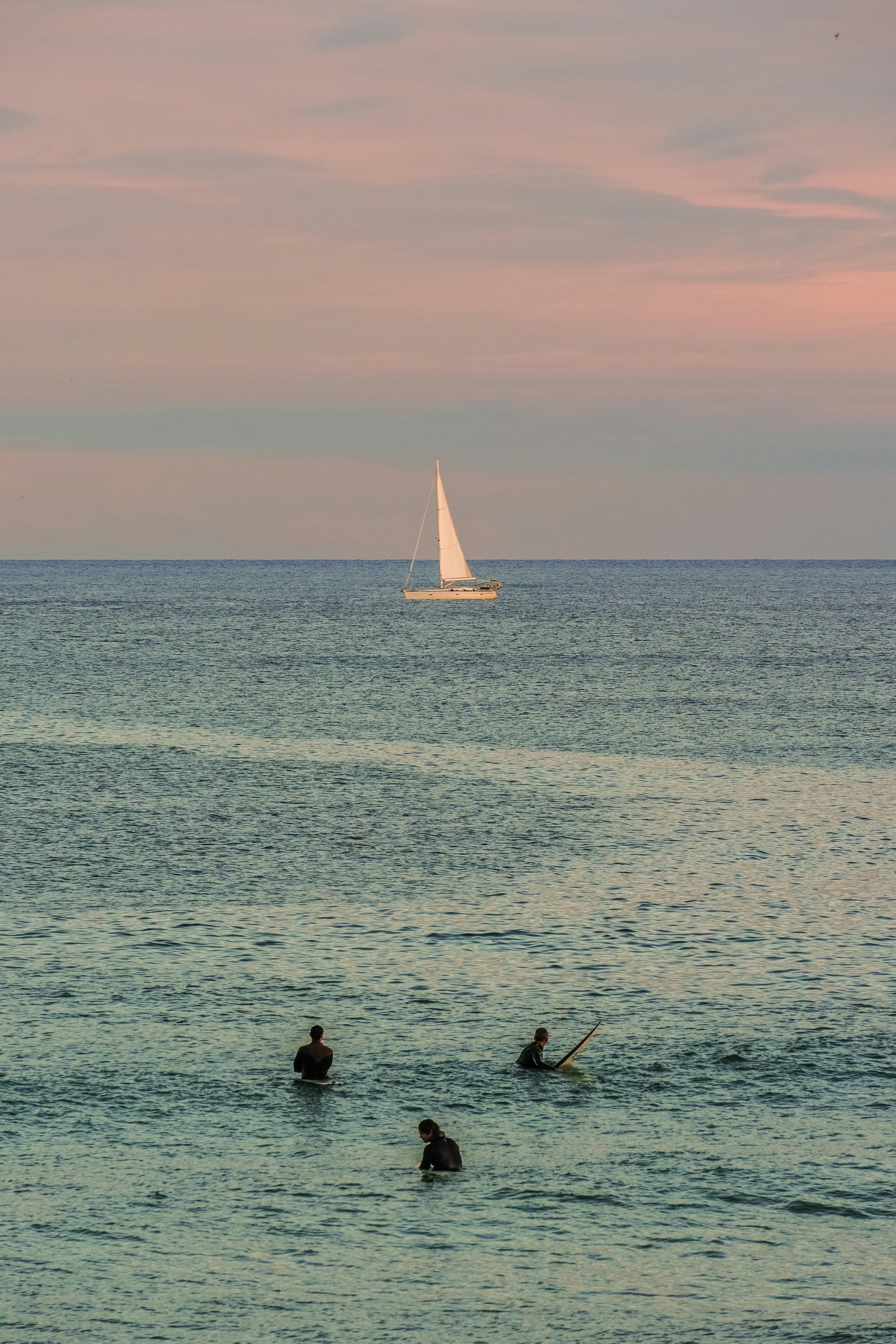 Sailboat on the ocean with surfers in-water surfers