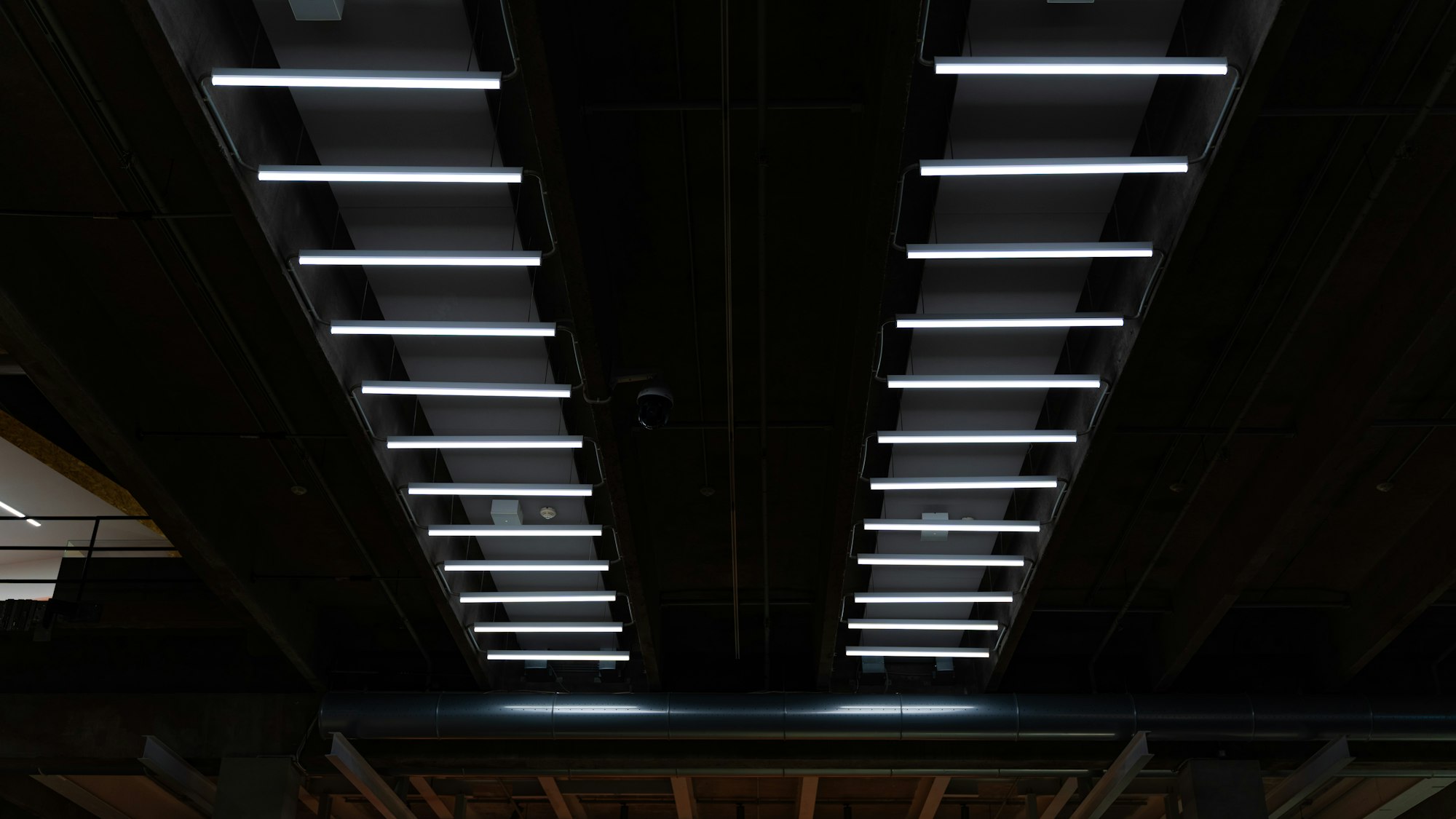 Rows of light fixtures on a dark industrial warehouse ceiling