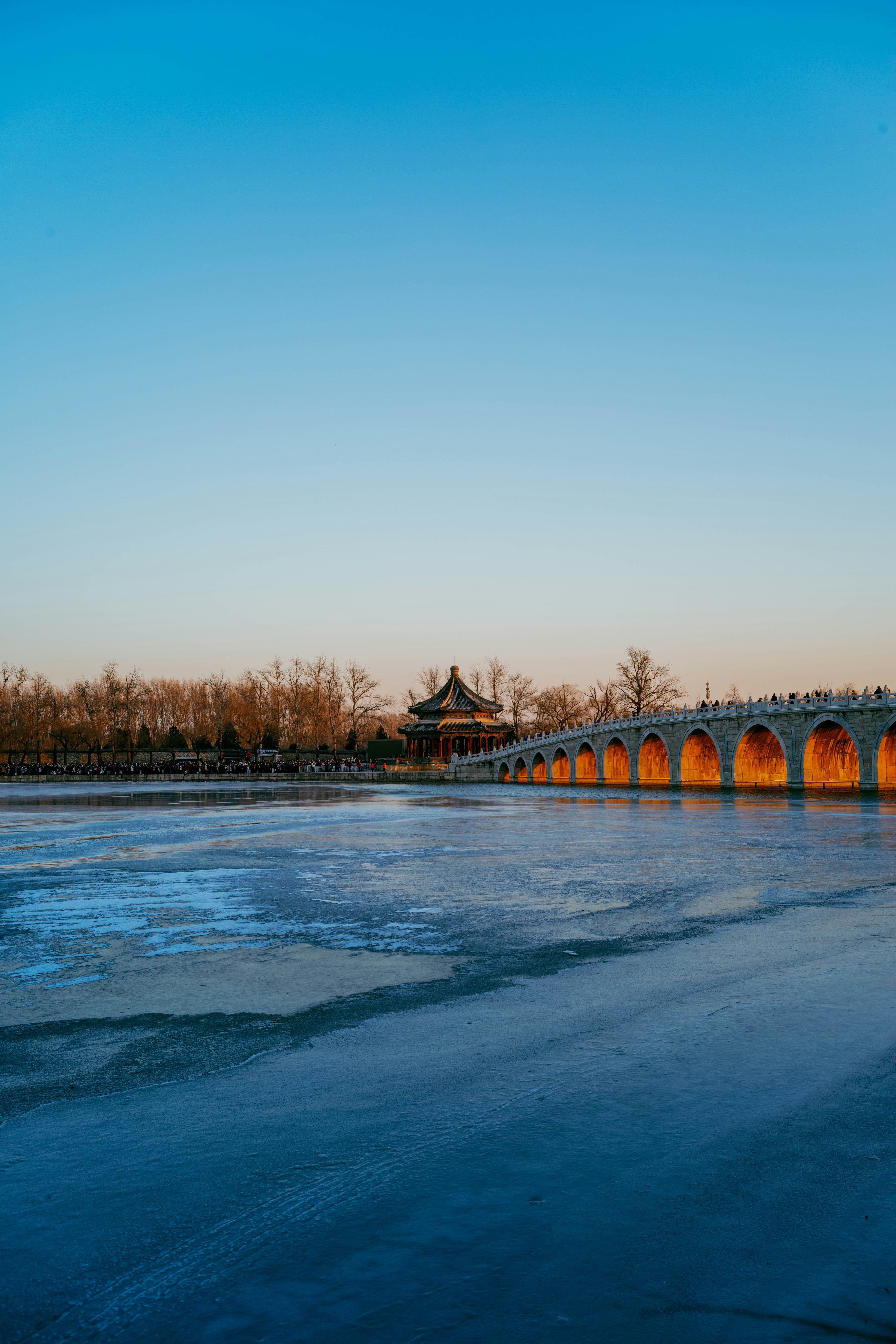 Arched bridge over a frozen lake at sunset