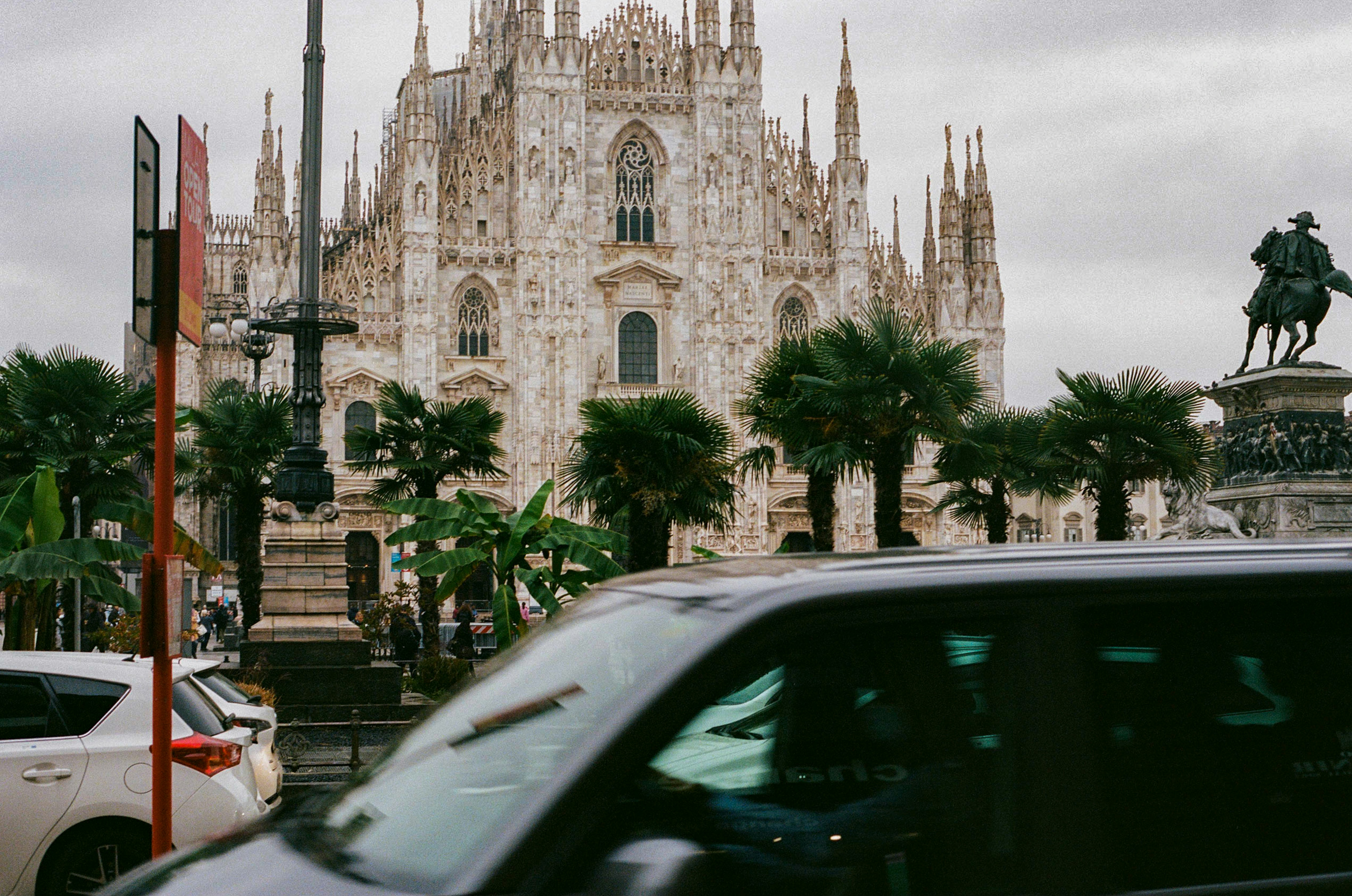 Milan cathedral with cars and statue in foreground