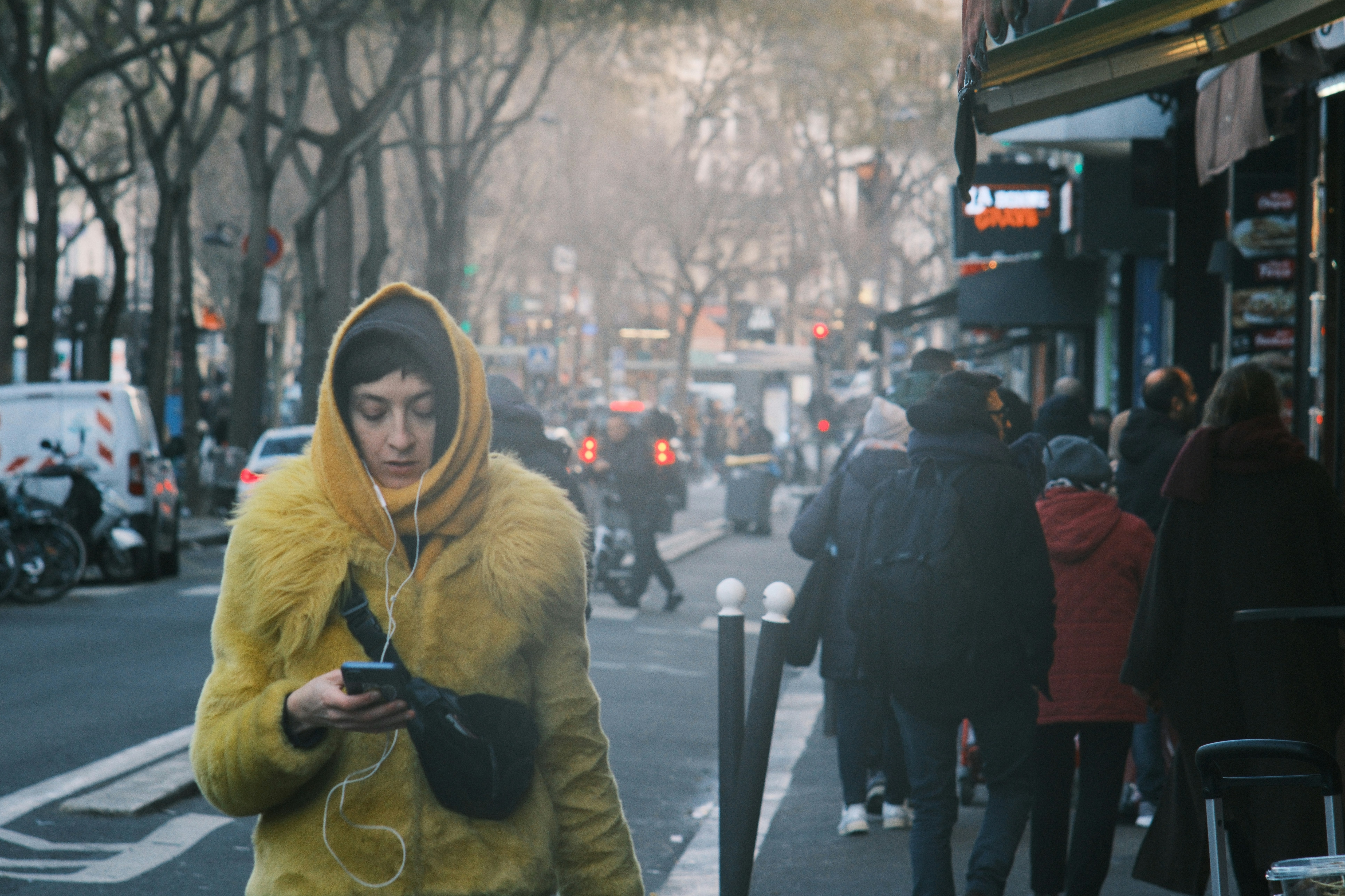Woman in yellow coat looking at phone on street
