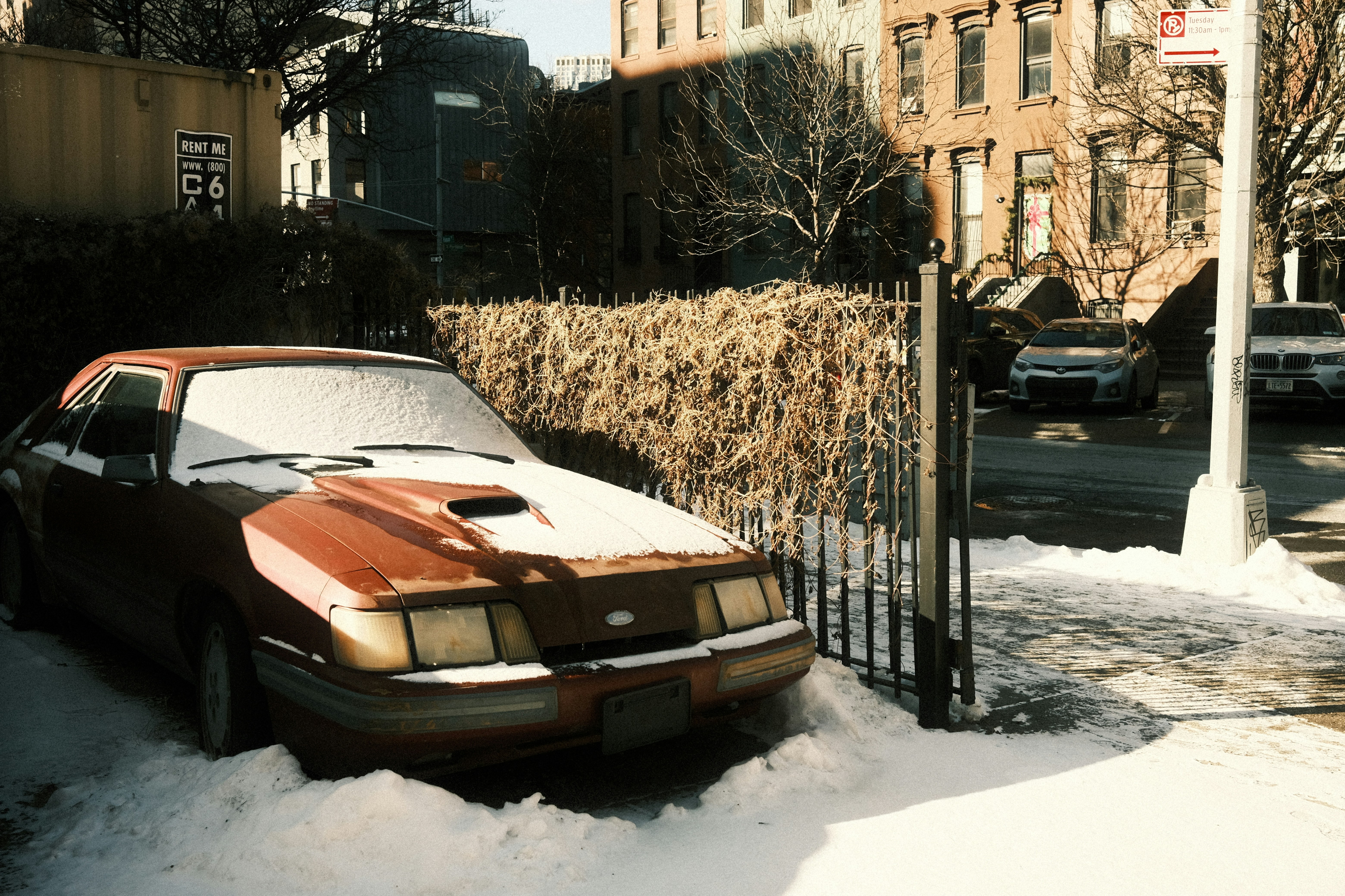Red car covered in snow on a street.