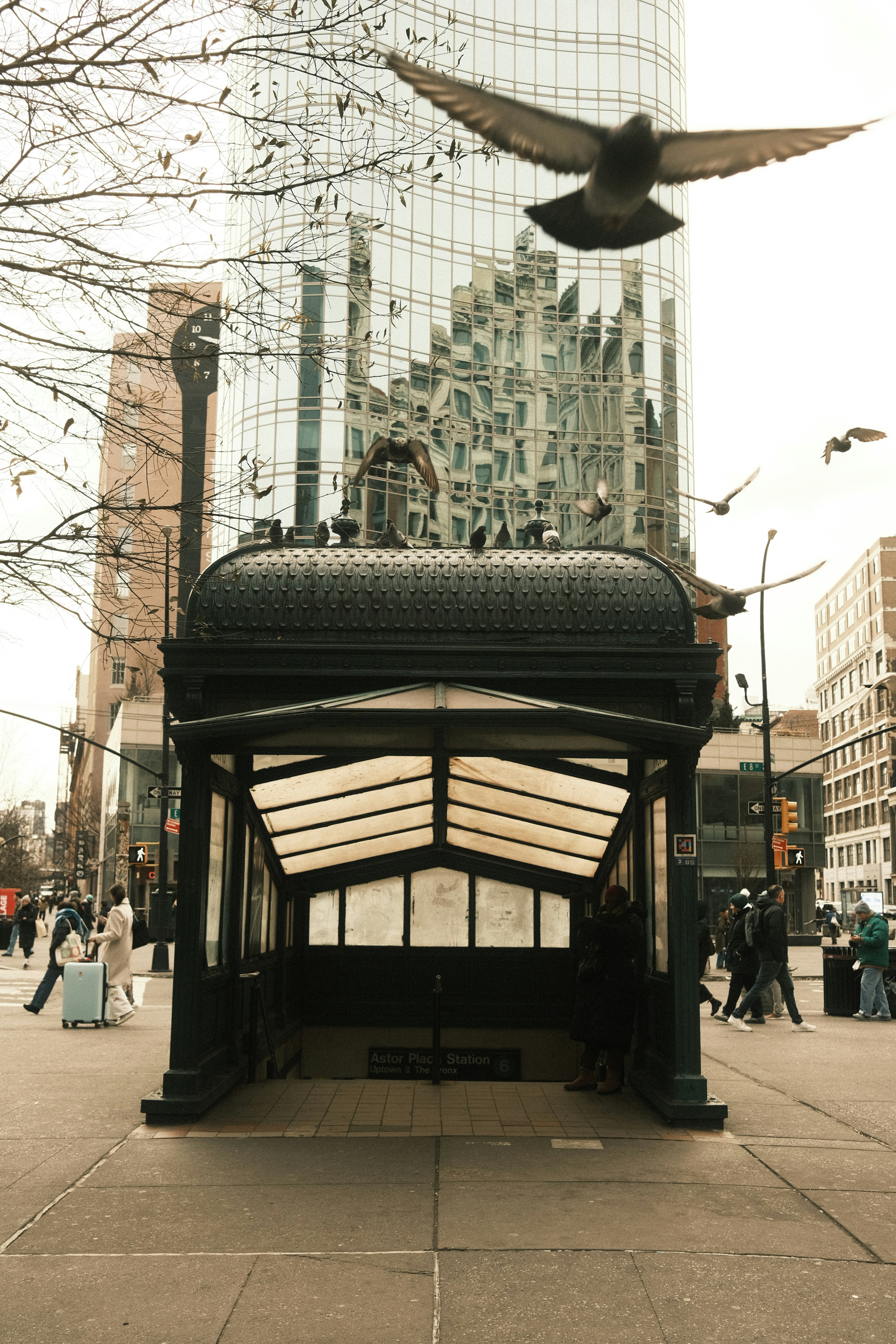 Pigeons fly near a historic subway entrance with modern buildings.