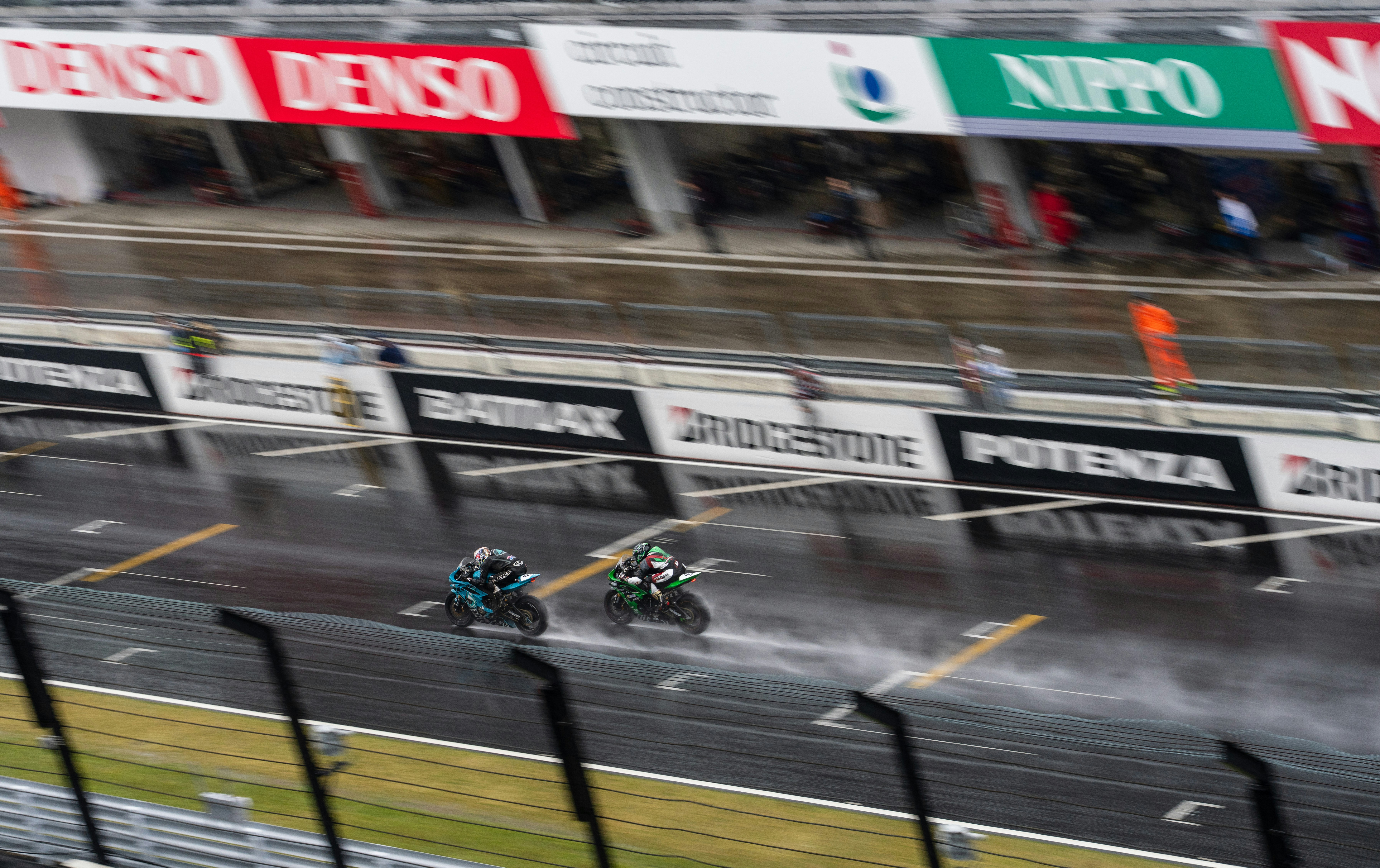 Motorcycles racing on a wet track during a race.