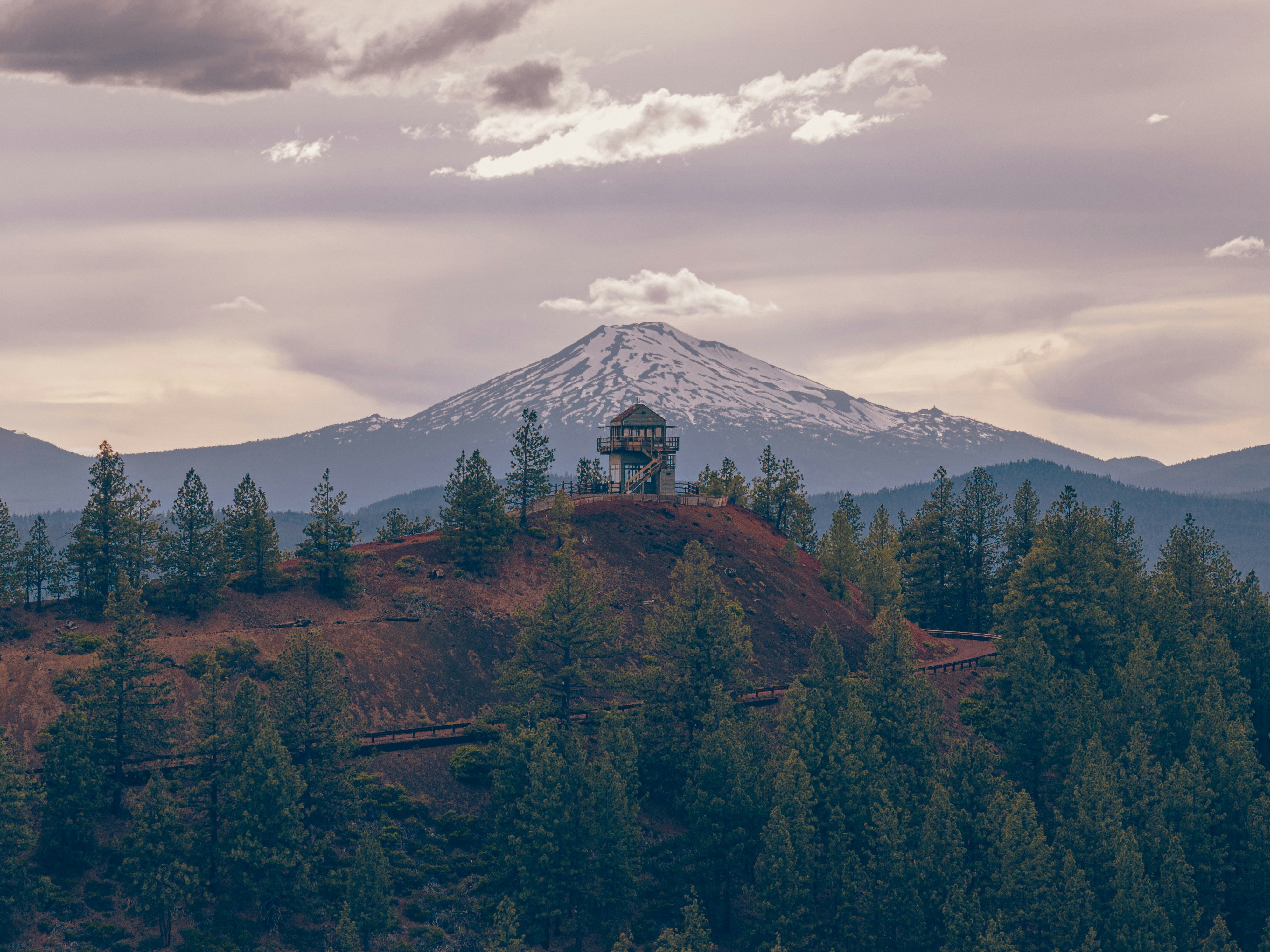 Snow-capped mountain behind a forest lookout tower.