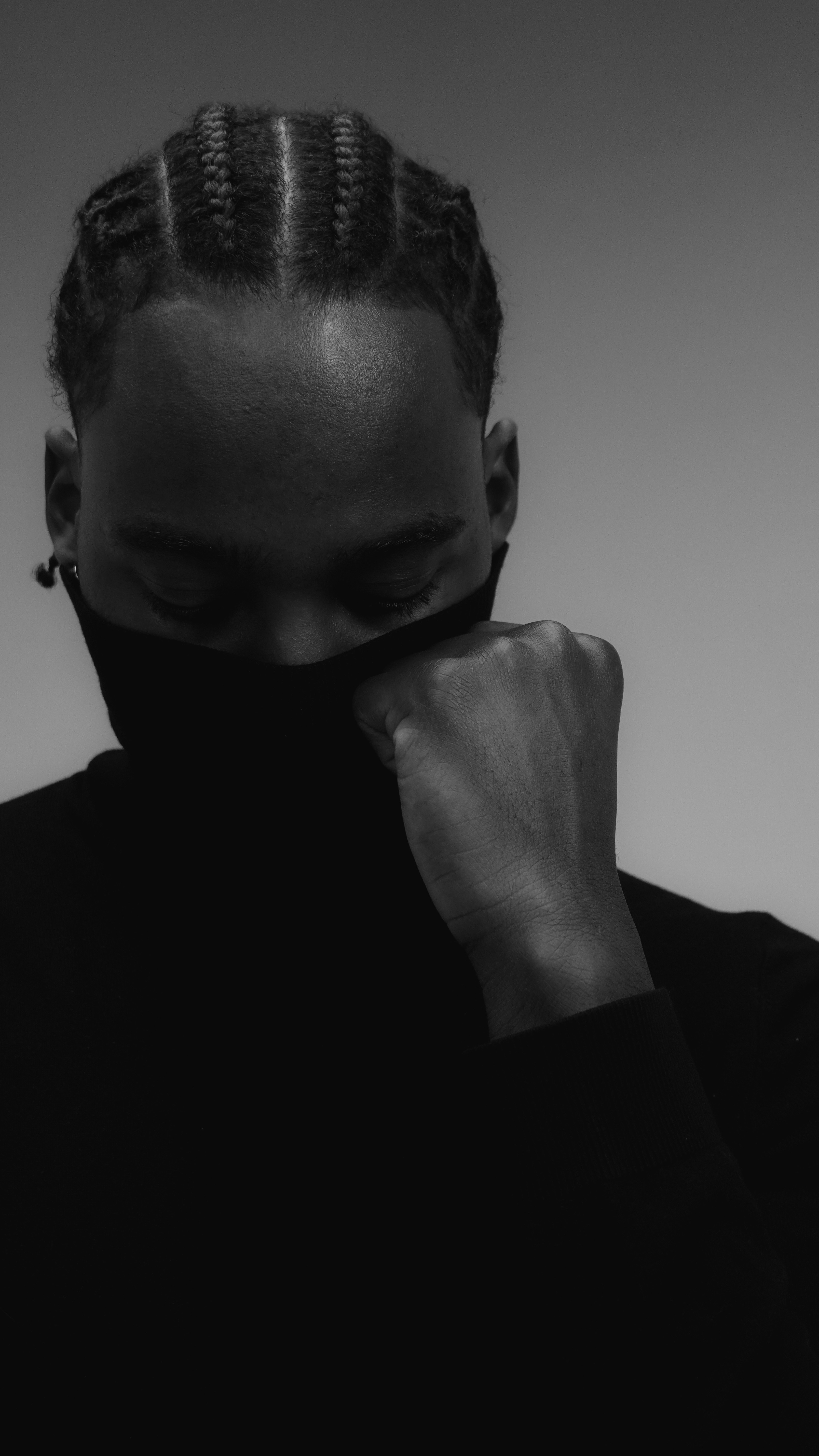 Man with braided hair wearing a black turtleneck and mask.