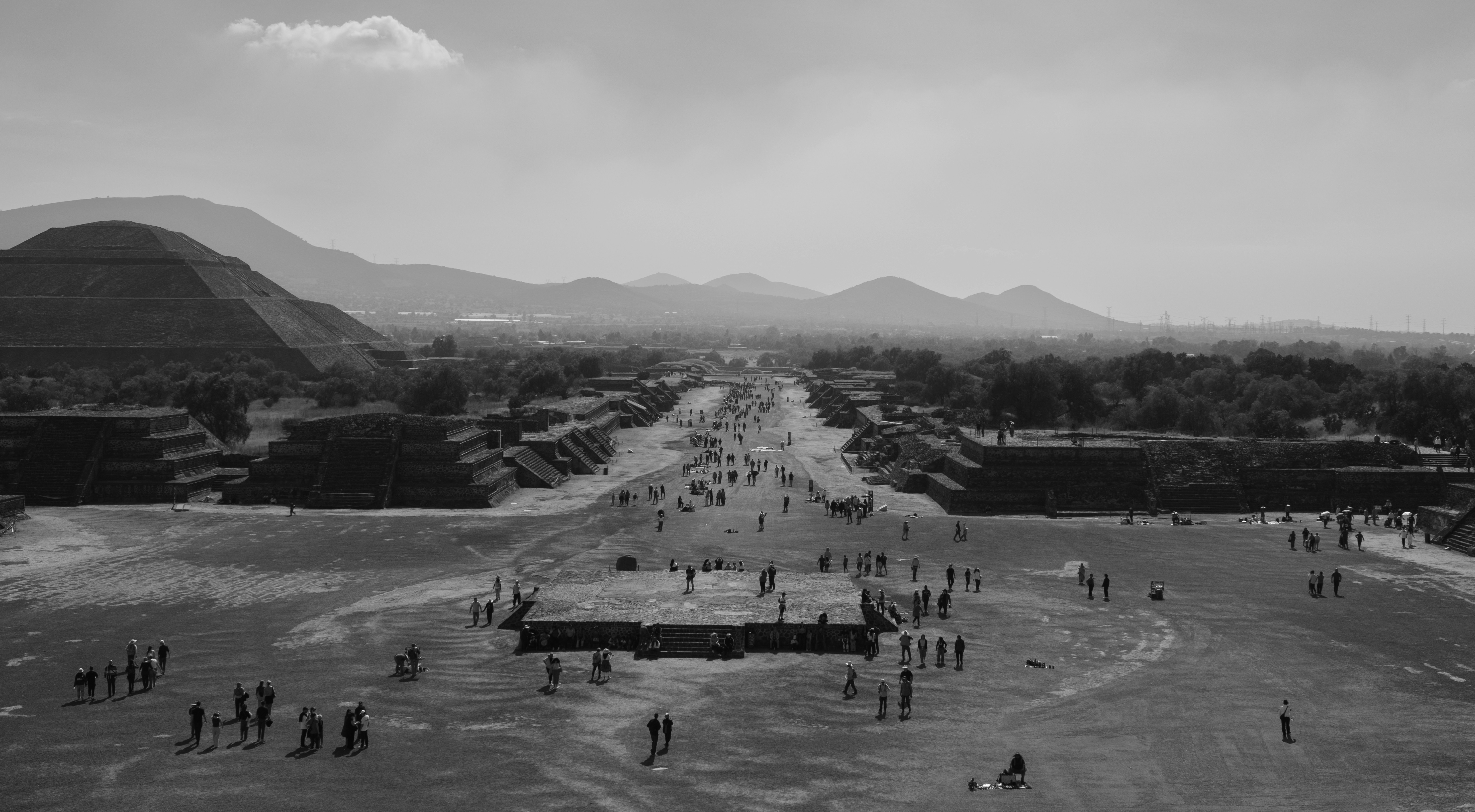 Ancient pyramids and people walking on a wide path.