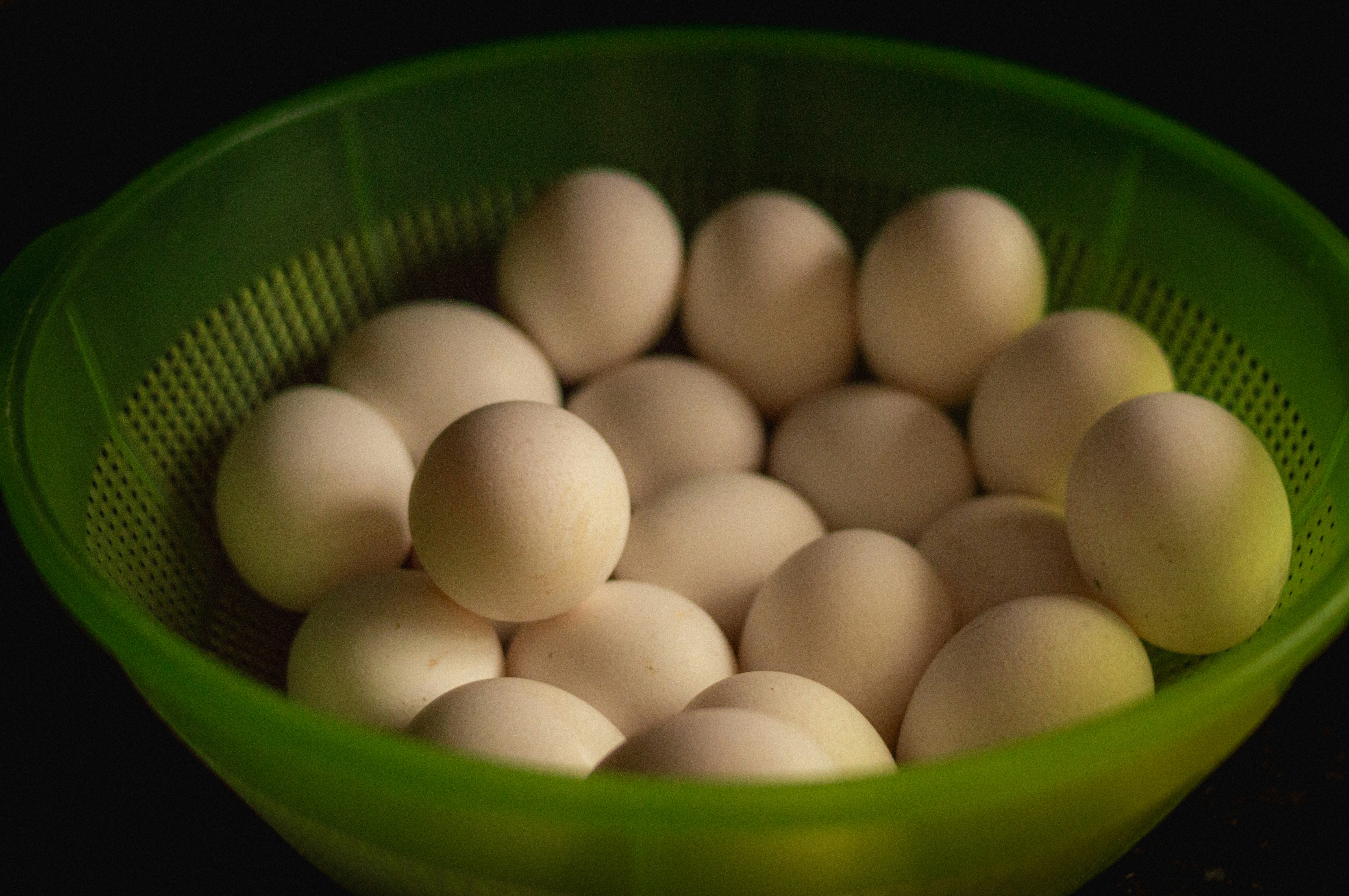 A green colander full of white eggs.