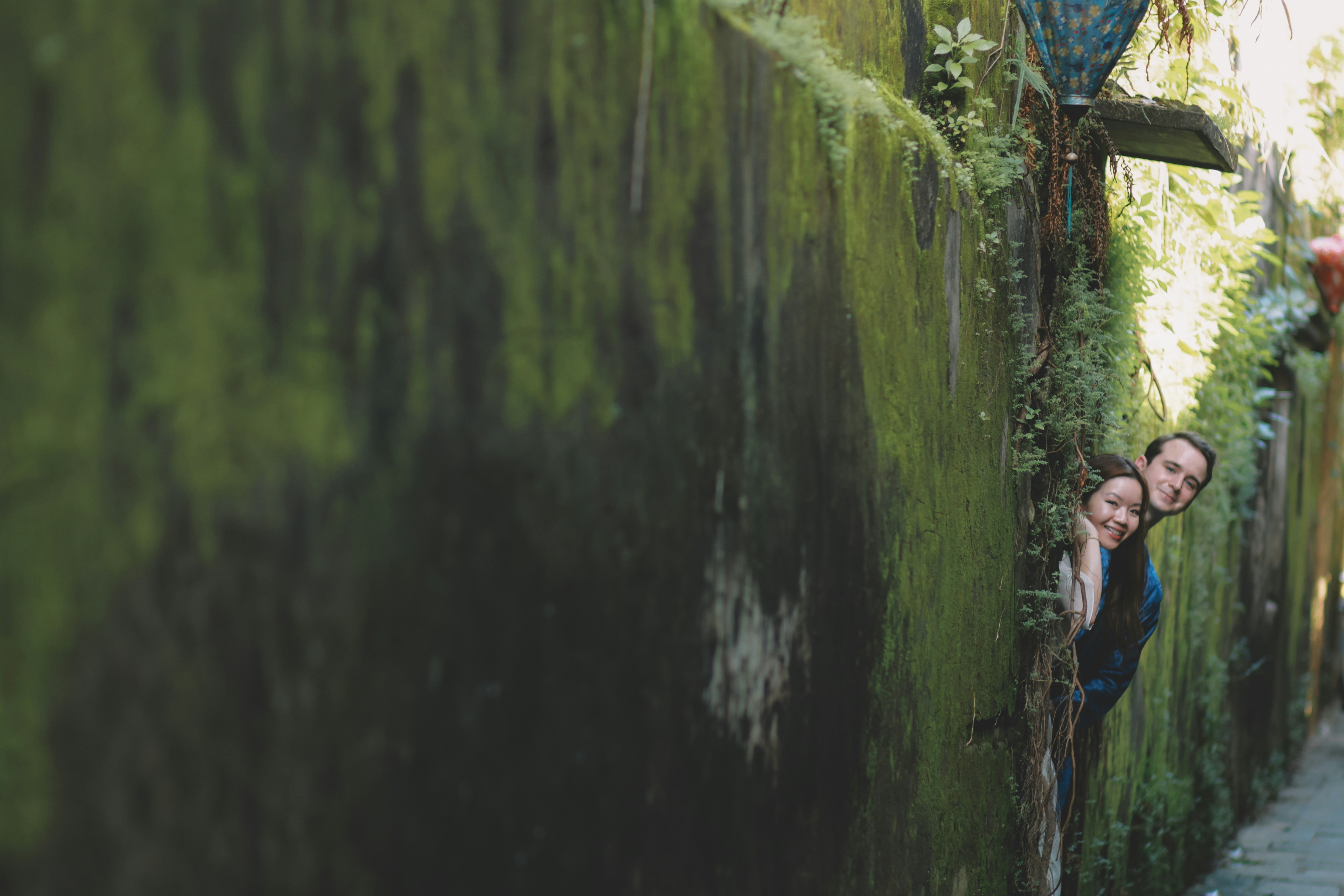 Couple peeking around a moss-covered wall