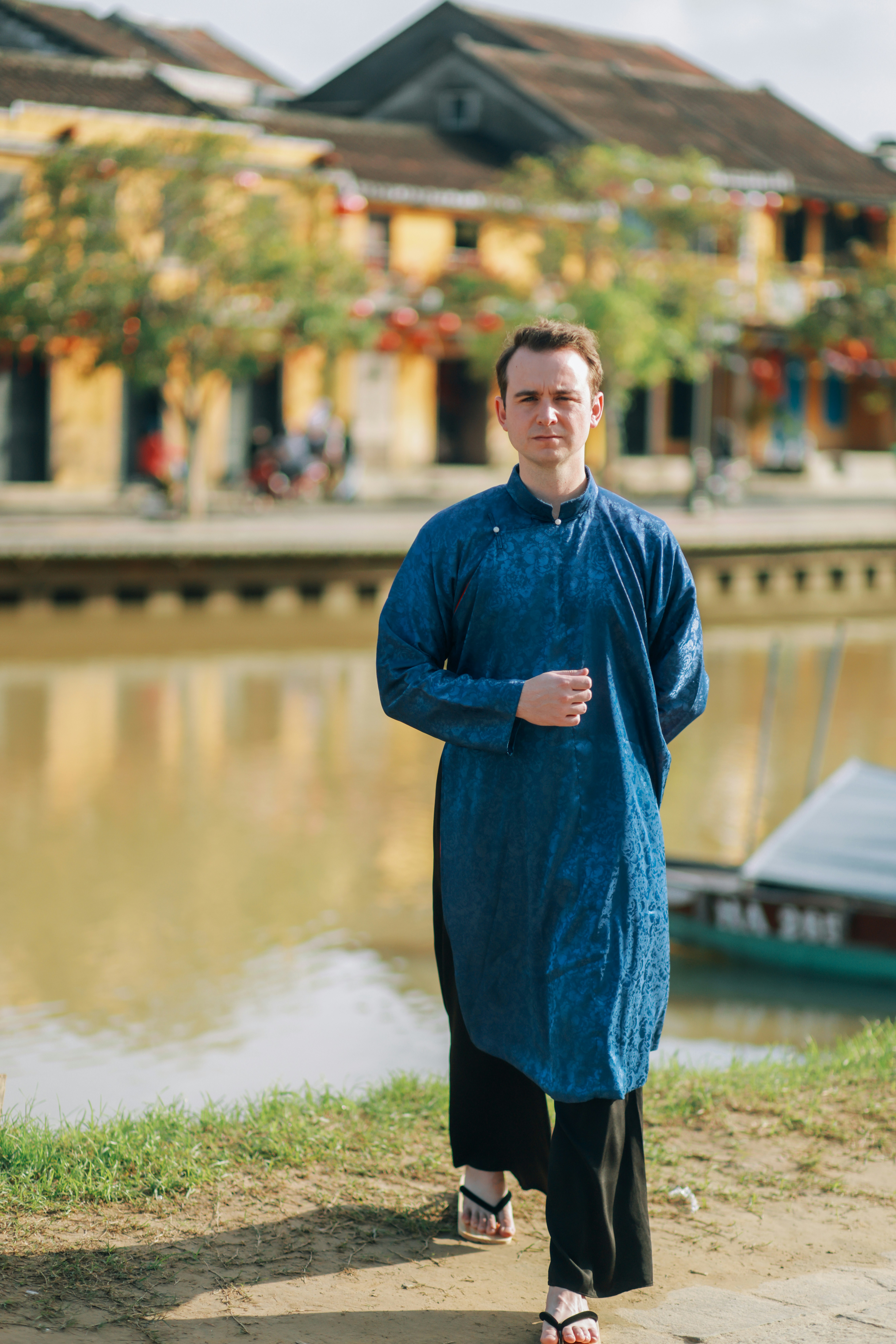 Man in blue traditional vietnamese clothing by river.
