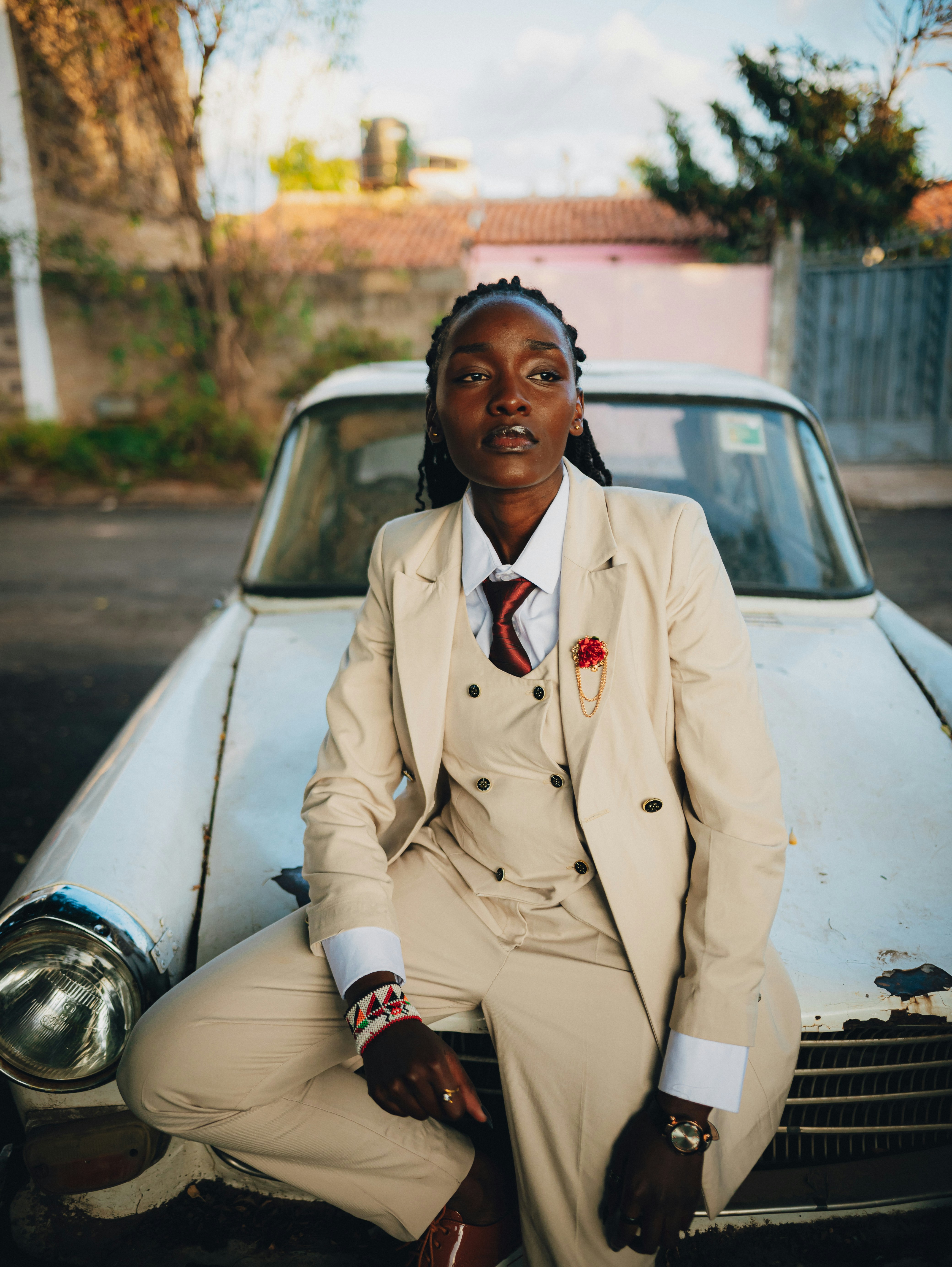 Woman in a tan suit sits on a vintage car.