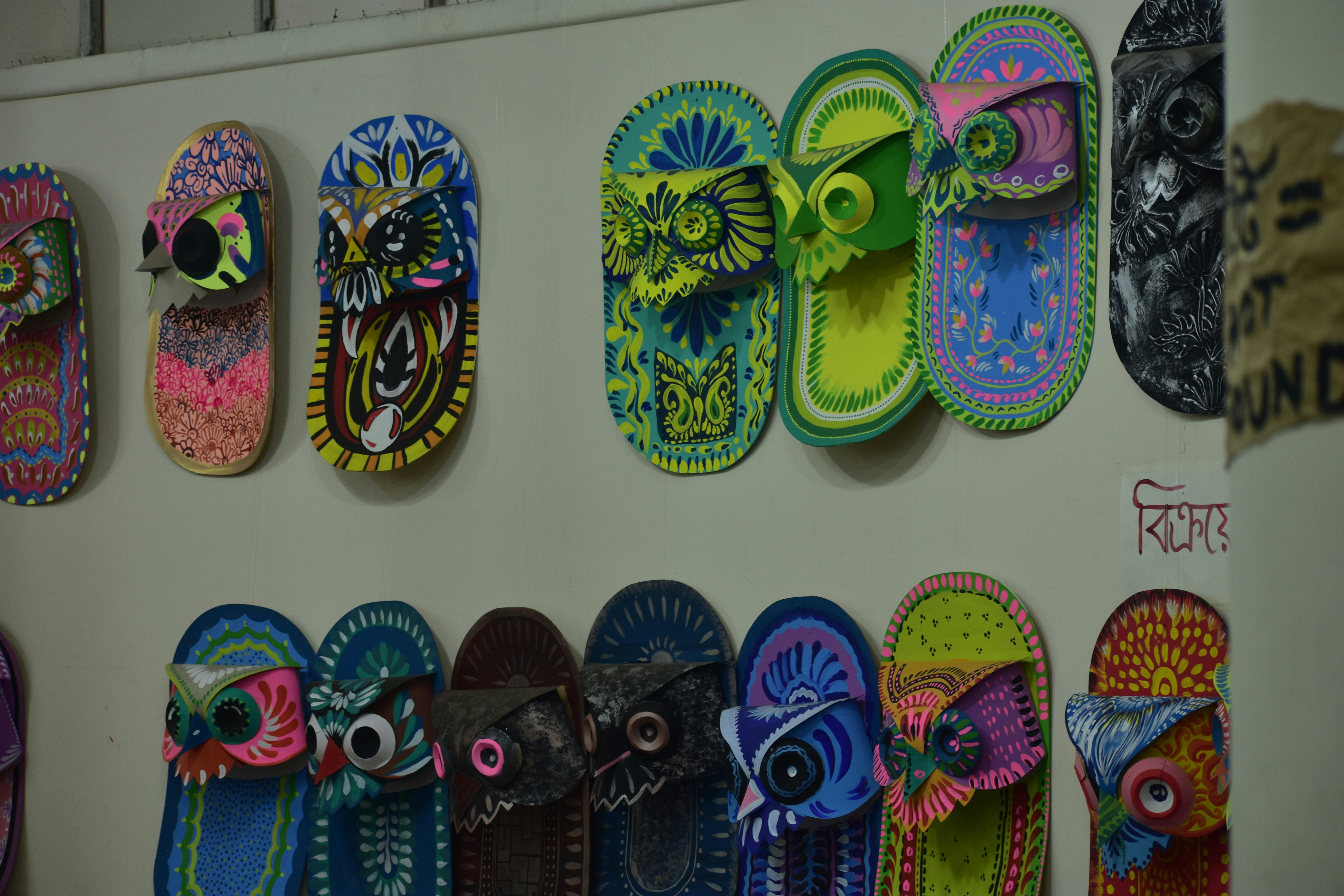 Colorful decorated flip-flops with owl designs displayed on wall