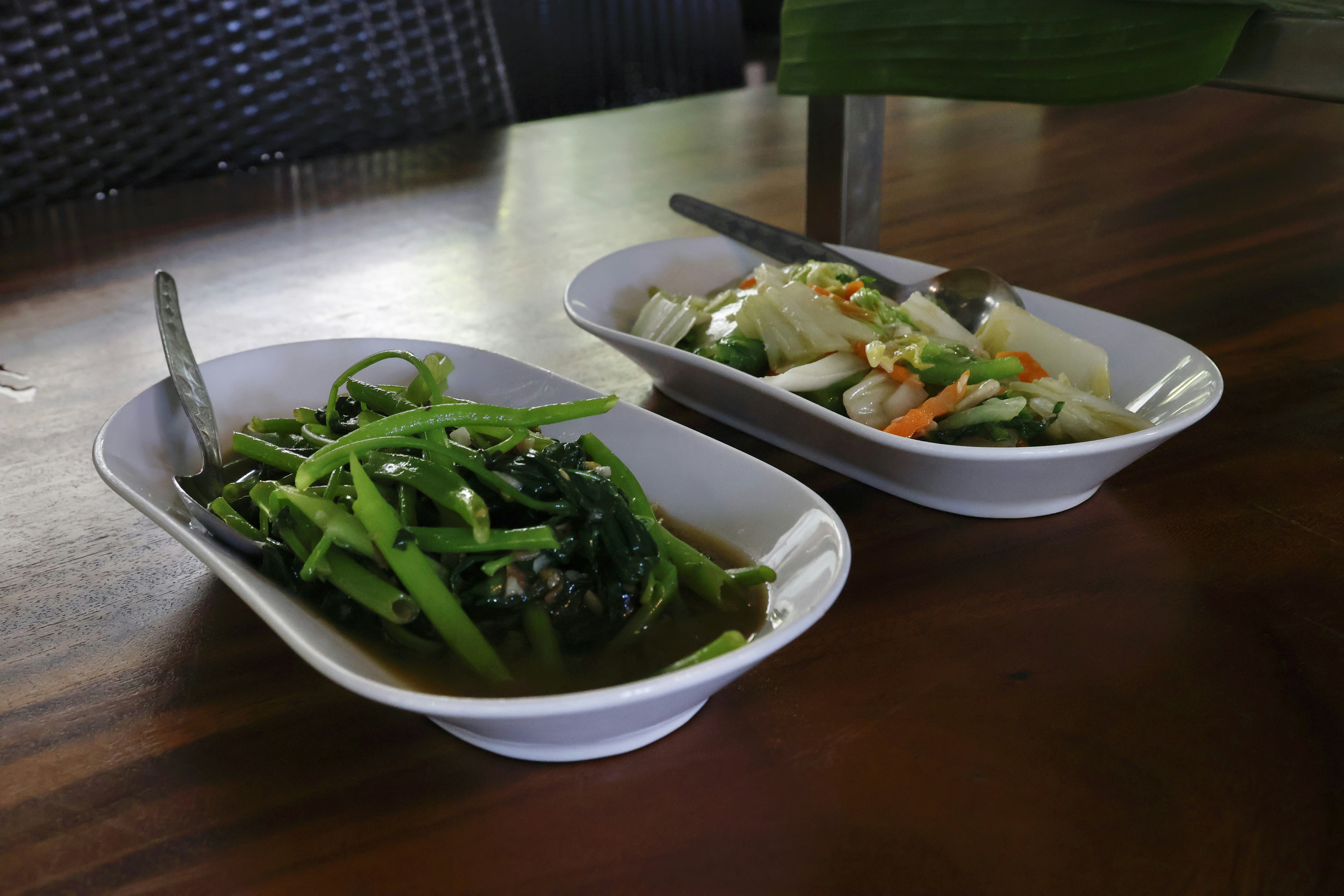 Two bowls of cooked vegetables on a wooden table.