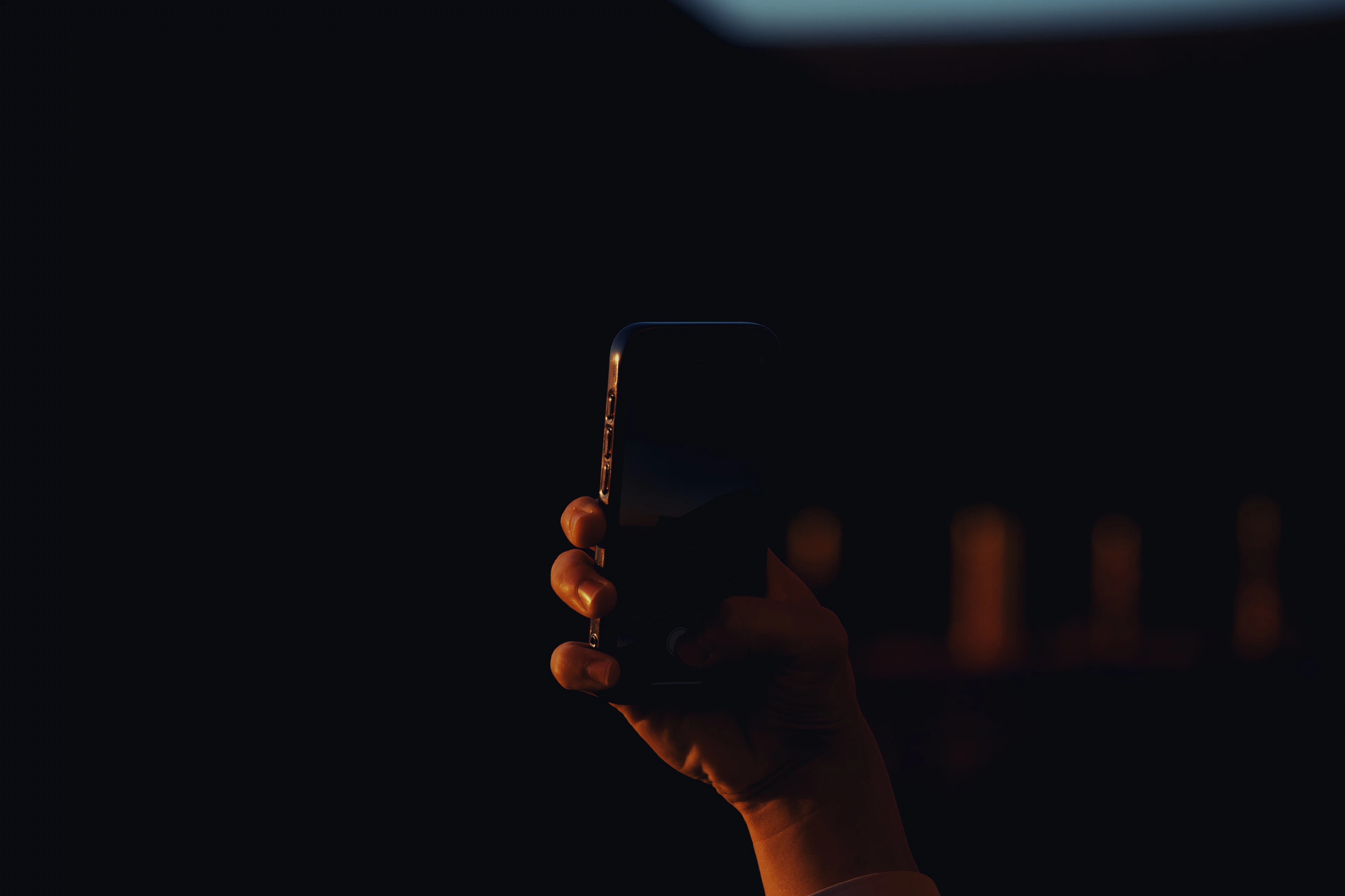 Hand holding up a smartphone in warm low light against a dark background