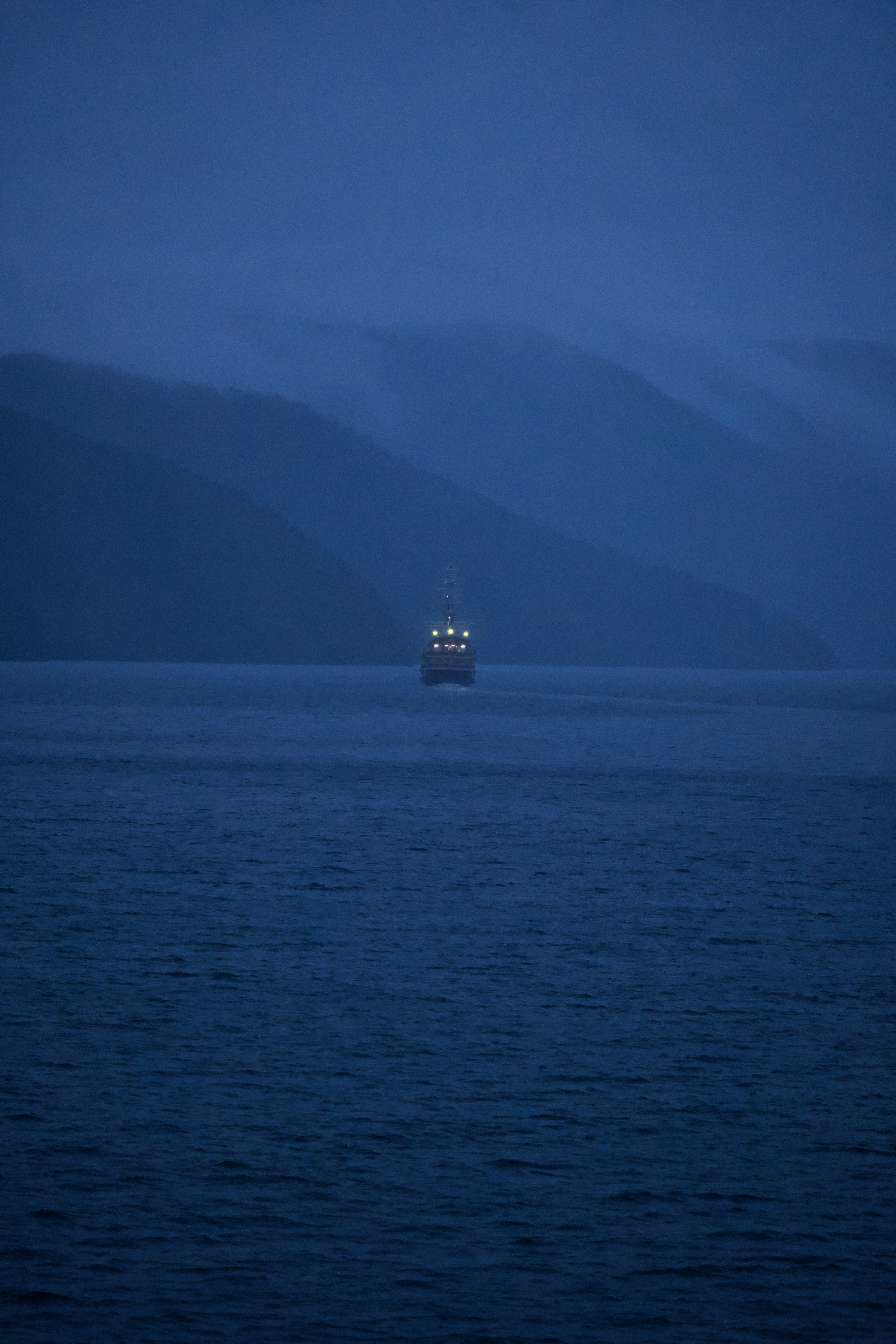 A lone ship sails on a misty, dark blue sea.