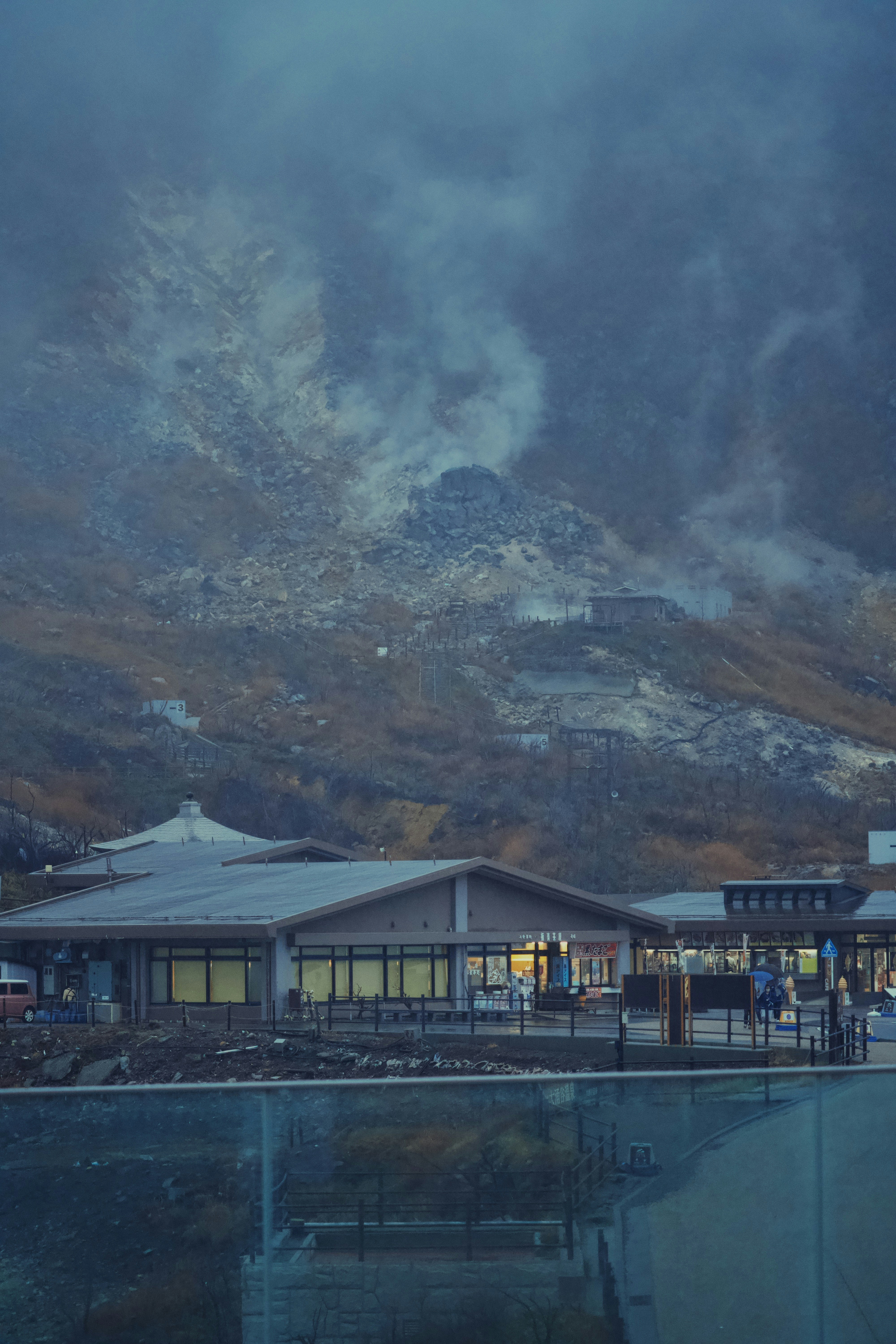Buildings nestled below a misty, volcanic mountainside.