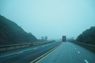 A truck drives on a foggy highway through hills.